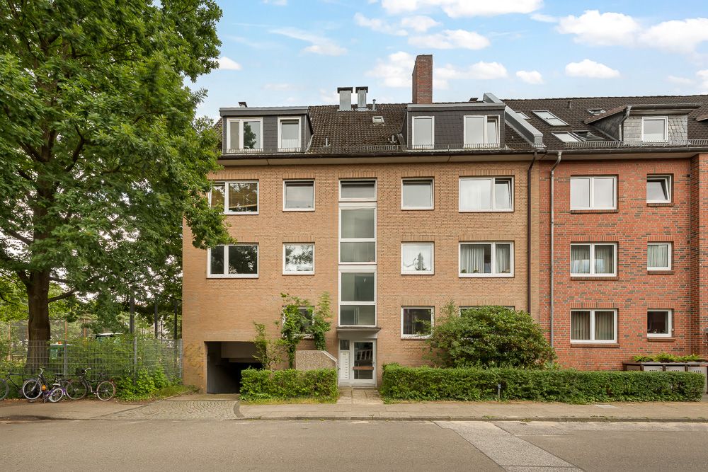 Mehrfamilienhaus mit vier Etagen, Ziegel-Fassade und begrüntem Eingangsbereich.