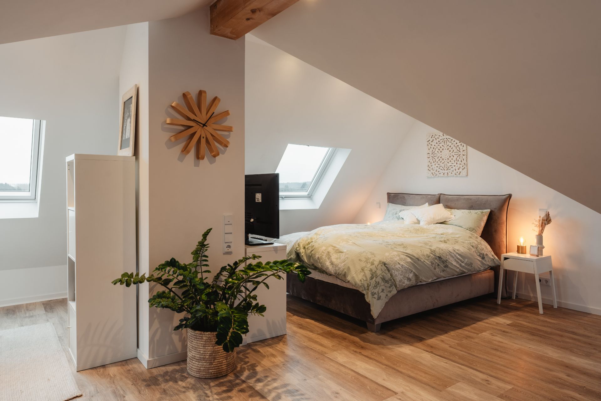 Modernes Schlafzimmer unter dem Dach mit Doppelbett, Dachfenster, Pflanze und Holzfußboden.