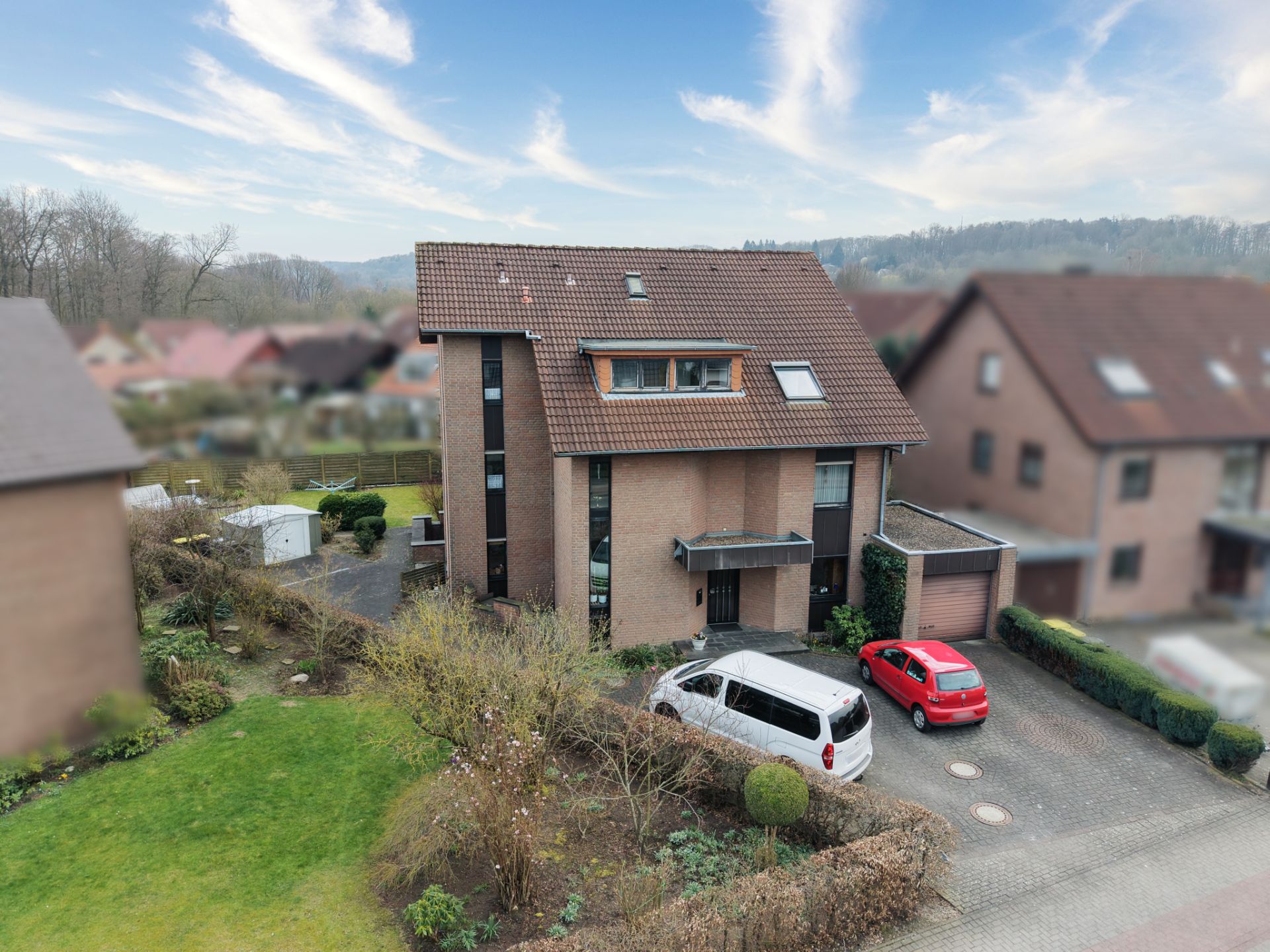 Zweistöckiges Wohnhaus mit rotem Dach, Garten und zwei parkenden Autos vor der Garage.