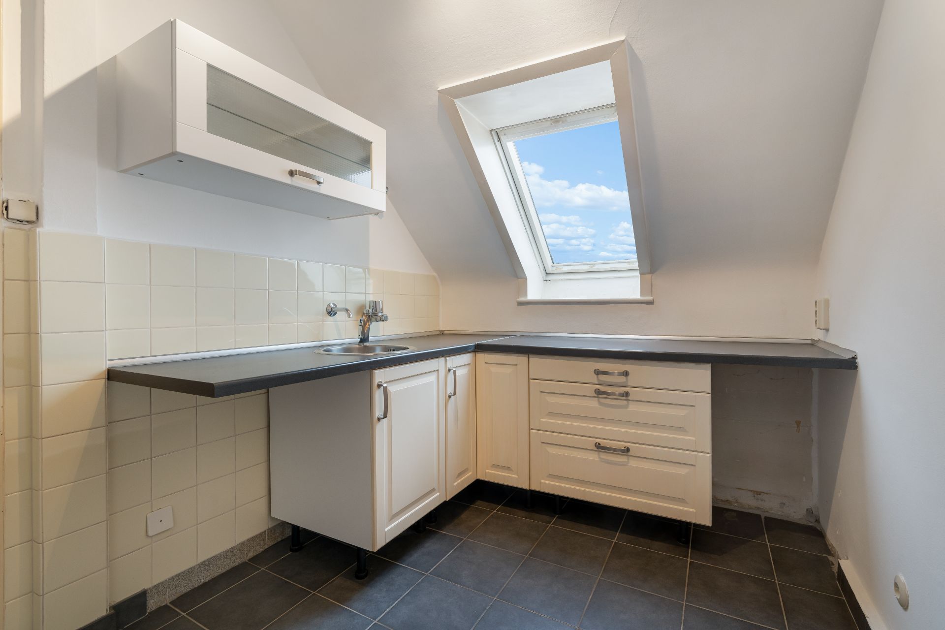 Kleine helle Einbauküche mit Dachfenster, weißem Schrank und dunkler Arbeitsplatte.