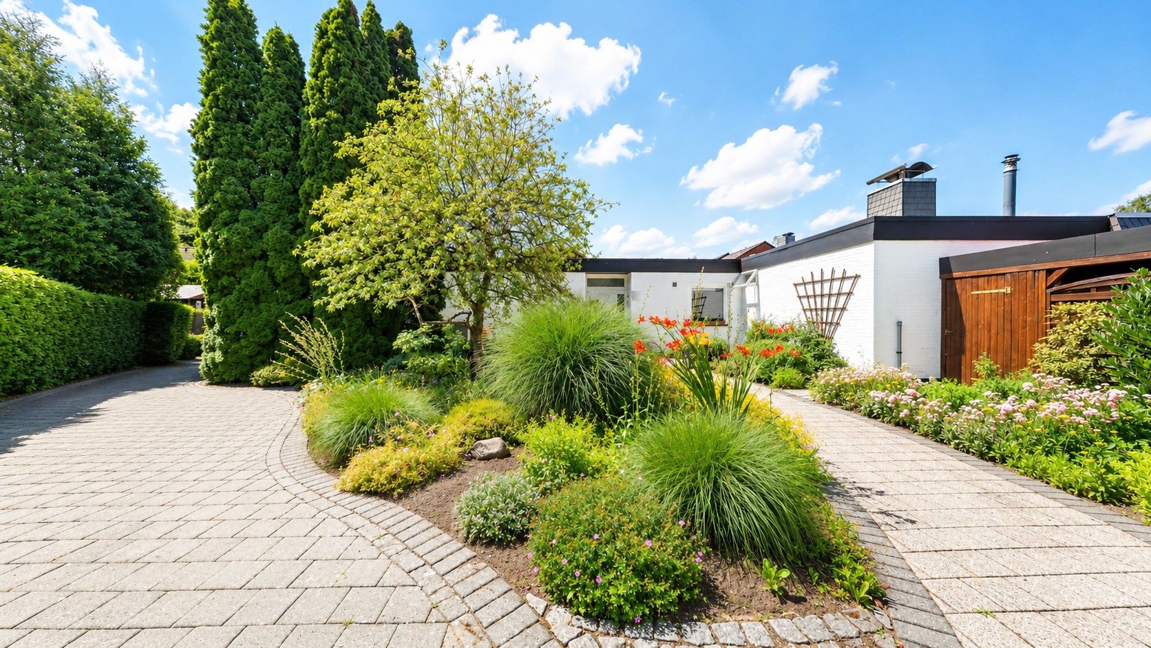 Gepflegter Garten mit Gehweg, Sträuchern, Bäumen und einem weißen Haus im Hintergrund.