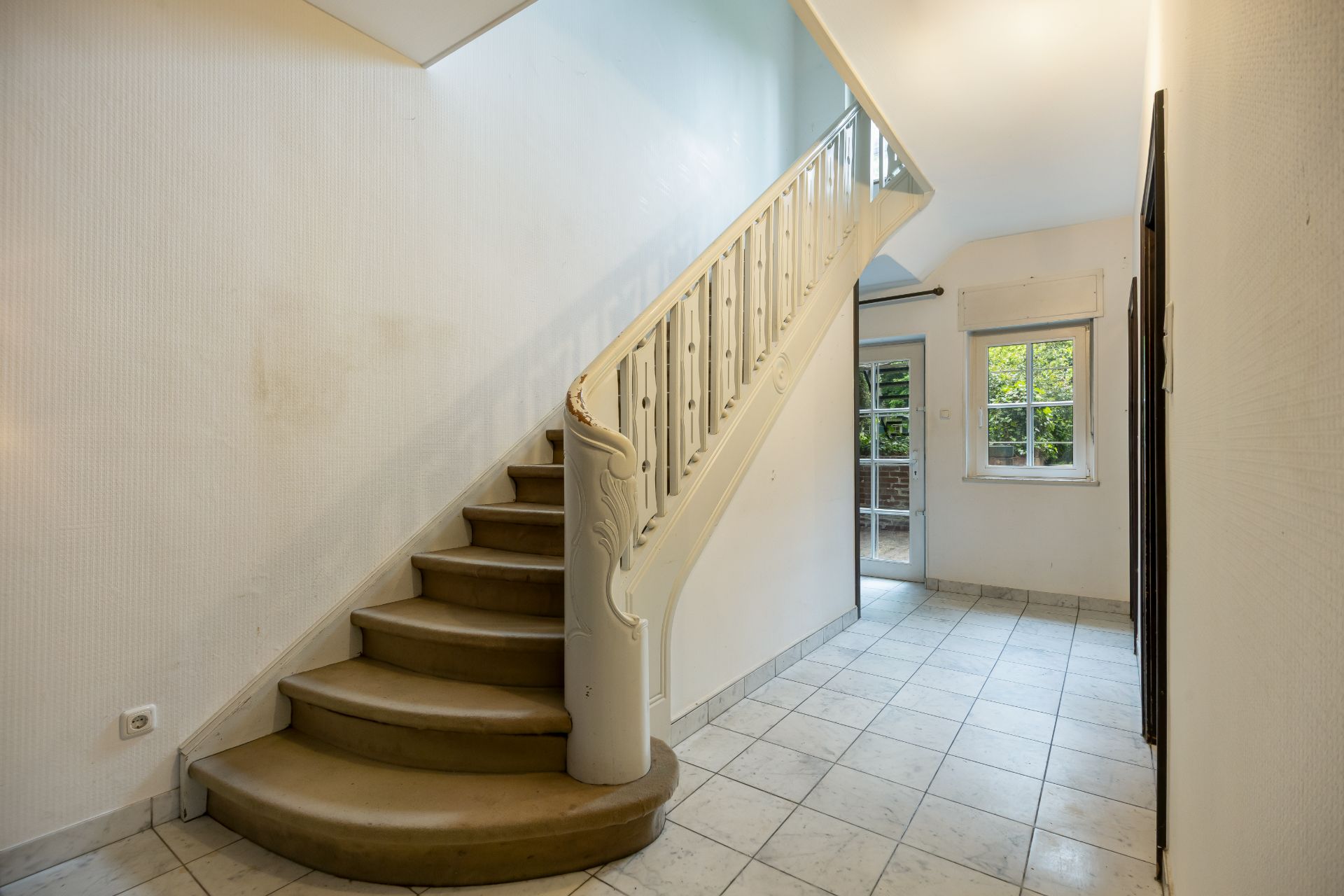 Heller Flur mit gefliesten Boden, Treppe und Fenster mit Blick auf den Garten.