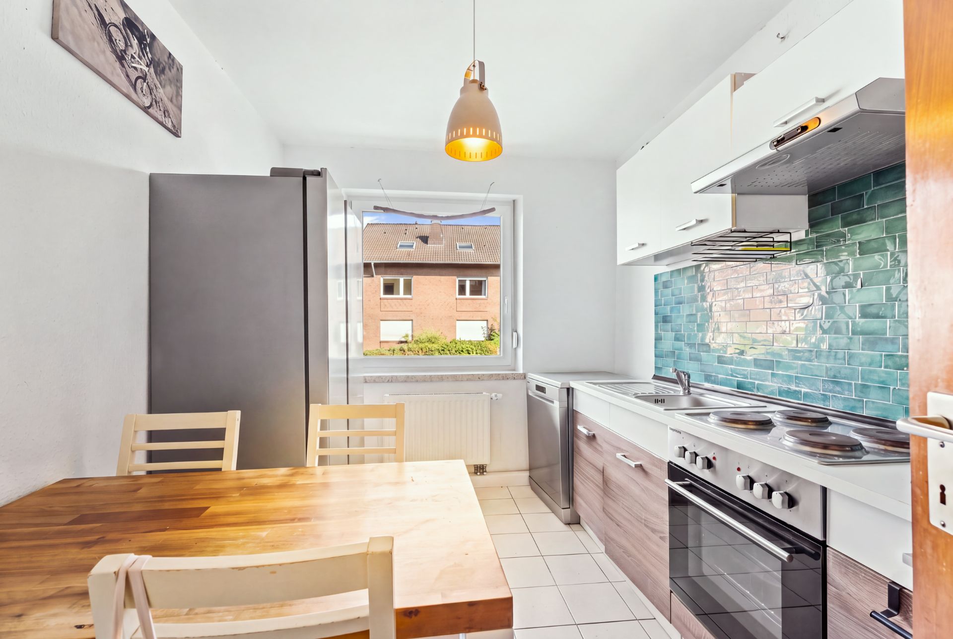 Helle Küche mit Holztisch, Stühlen, Herd, Kühlschrank und offenem Fenster.