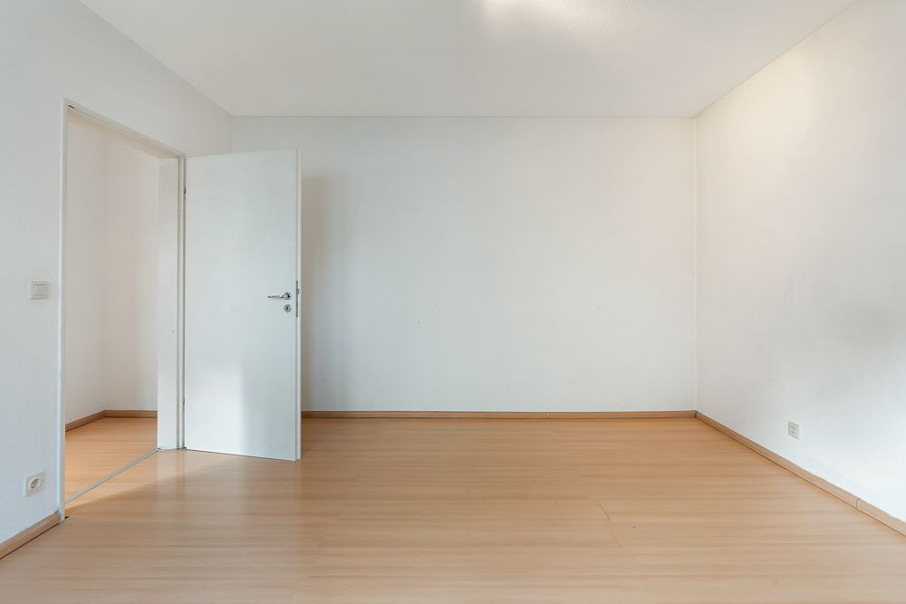 Leerer Raum mit hellen Holzböden, weißen Wänden und einer offenen Tür.