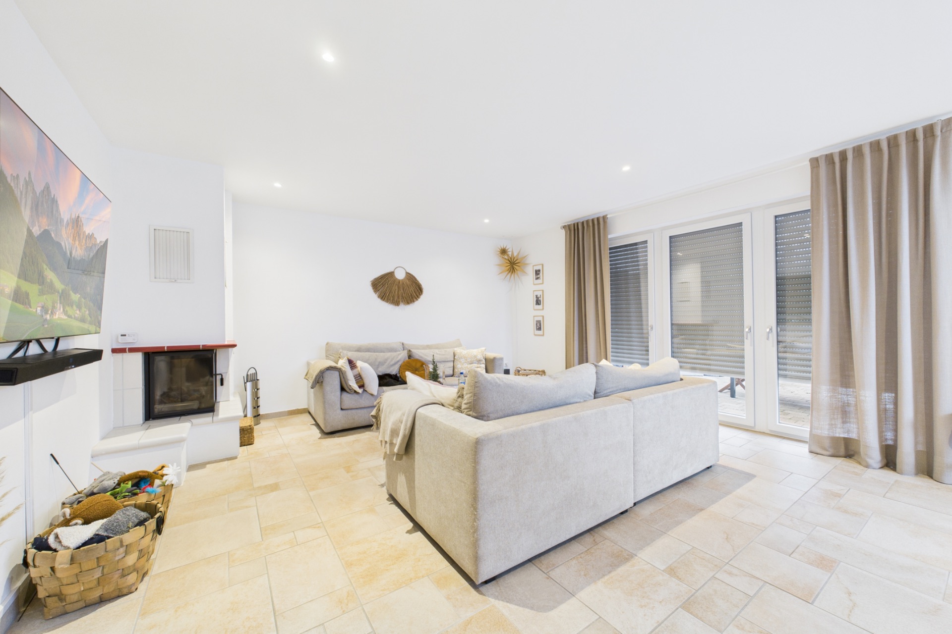 Helles Wohnzimmer mit zwei Sofas, Kamin, Fernseher und großen Fenstern mit Vorhängen.