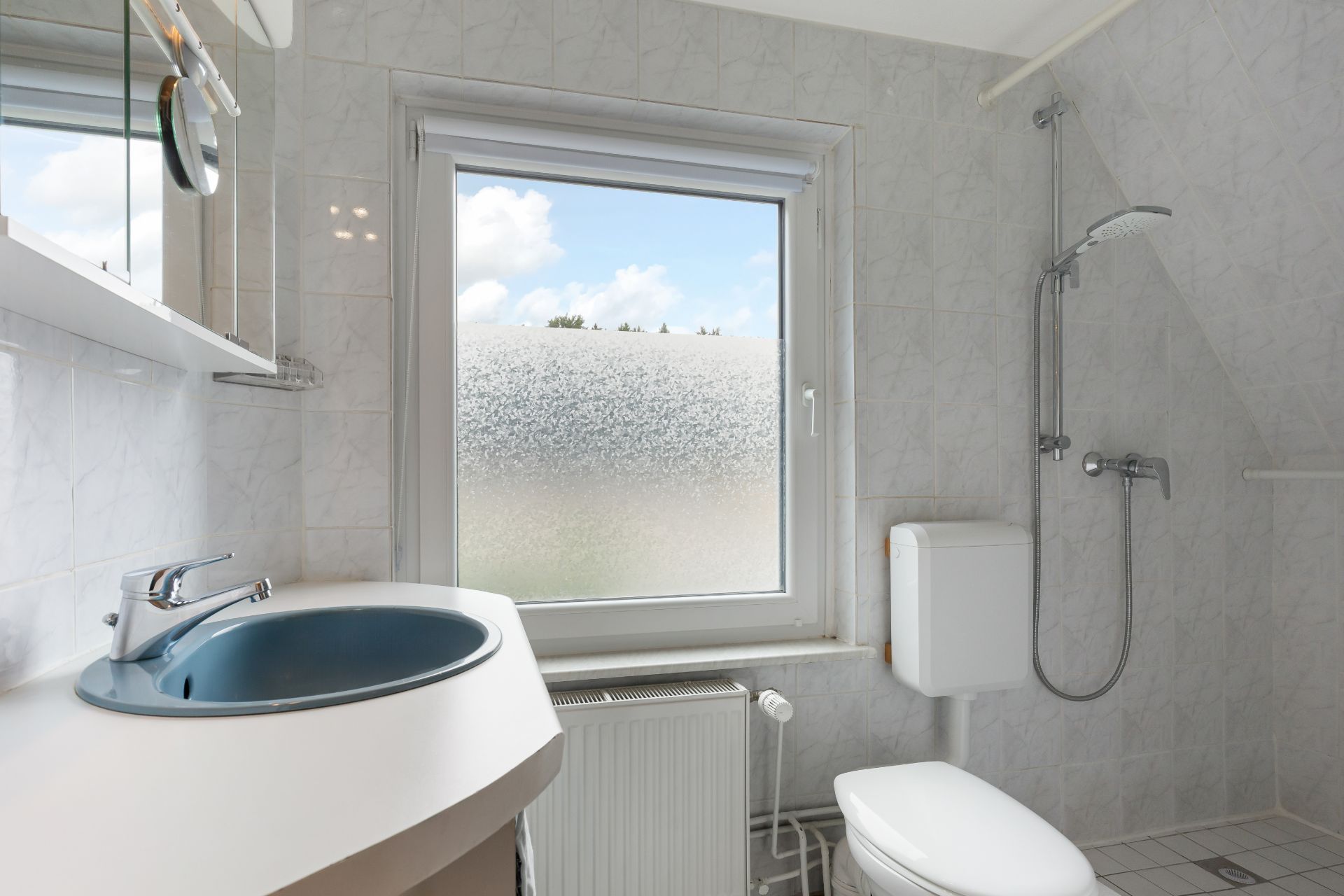 Helles Badezimmer mit Waschbecken, Toilette, Fenster und offener Dusche.