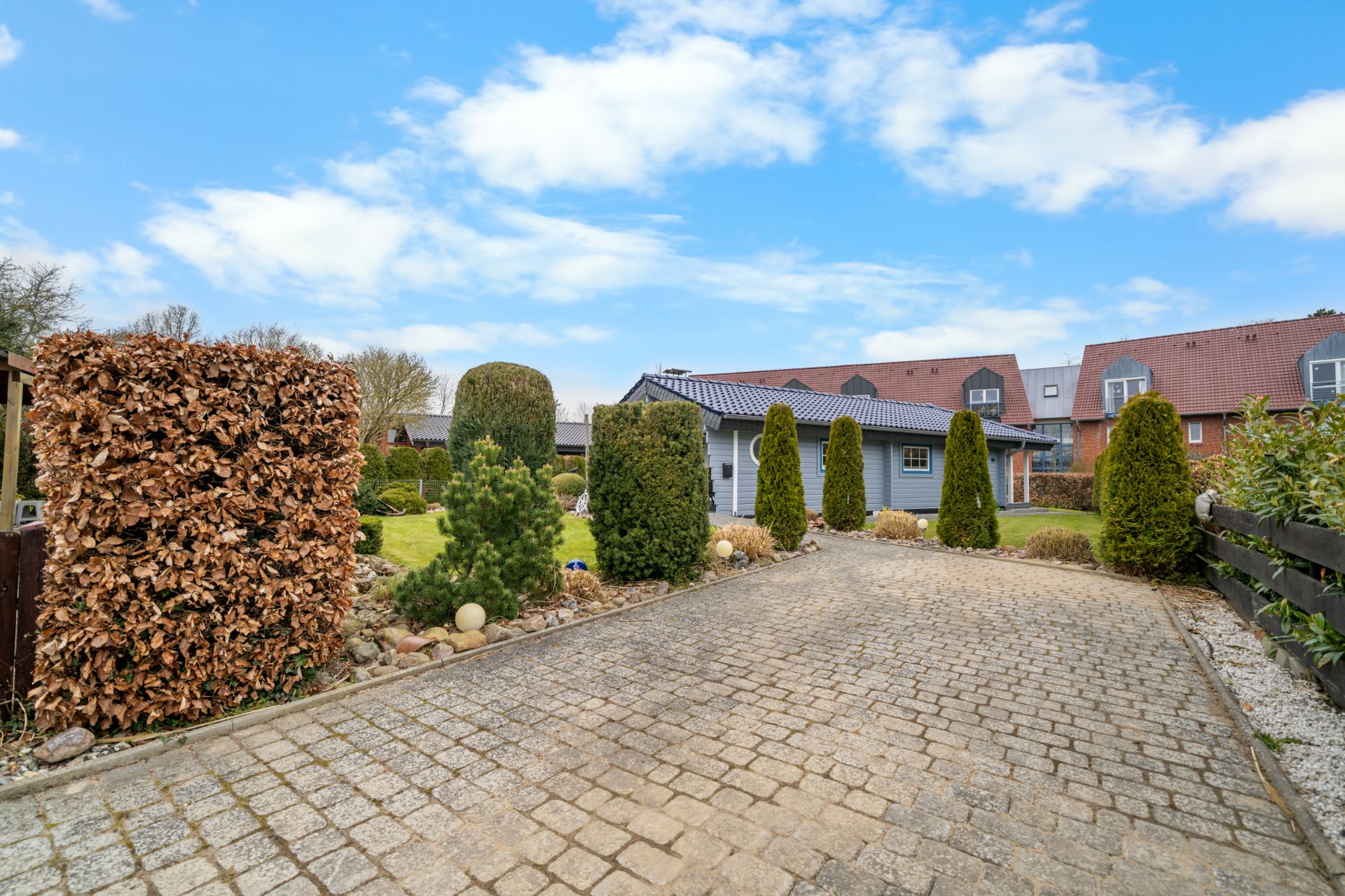 Gepflasterter Weg zu einem Haus mit gepflegtem Garten und Hecken an den Seiten.