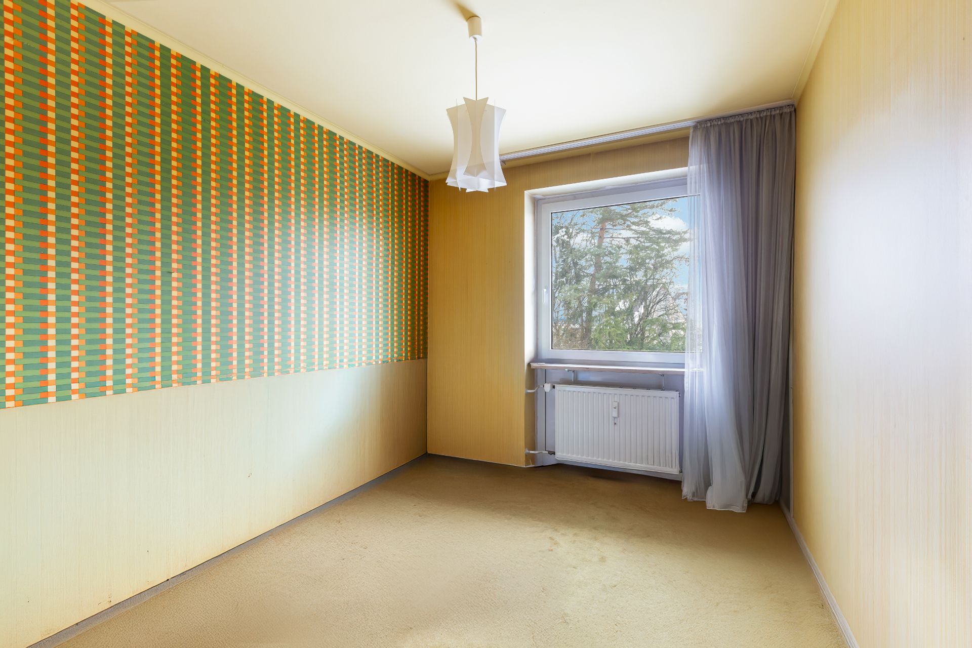 Leeres Zimmer mit gemusterter Tapete, gelbem Teppich und Fenster mit Vorhang.