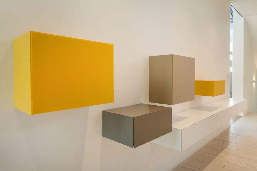 Mehrere bunte, wandmontierte Würfelschränke an einer weißen Wand in einem Flur.