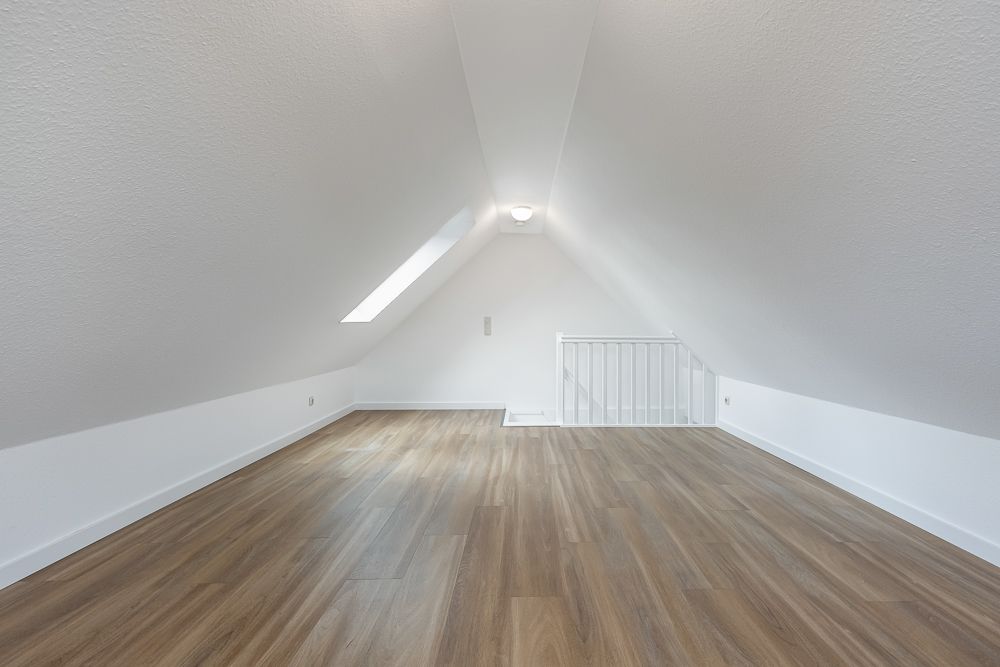 Leerer Dachbodenraum mit schrägen Wänden, Dachfenster und Holzfußboden.