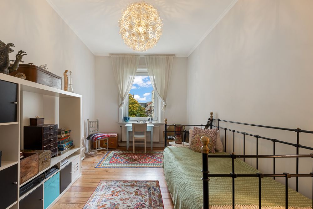 Helles Schlafzimmer mit Einzelbett, Regal, Schreibtisch am Fenster und Holzfußboden.