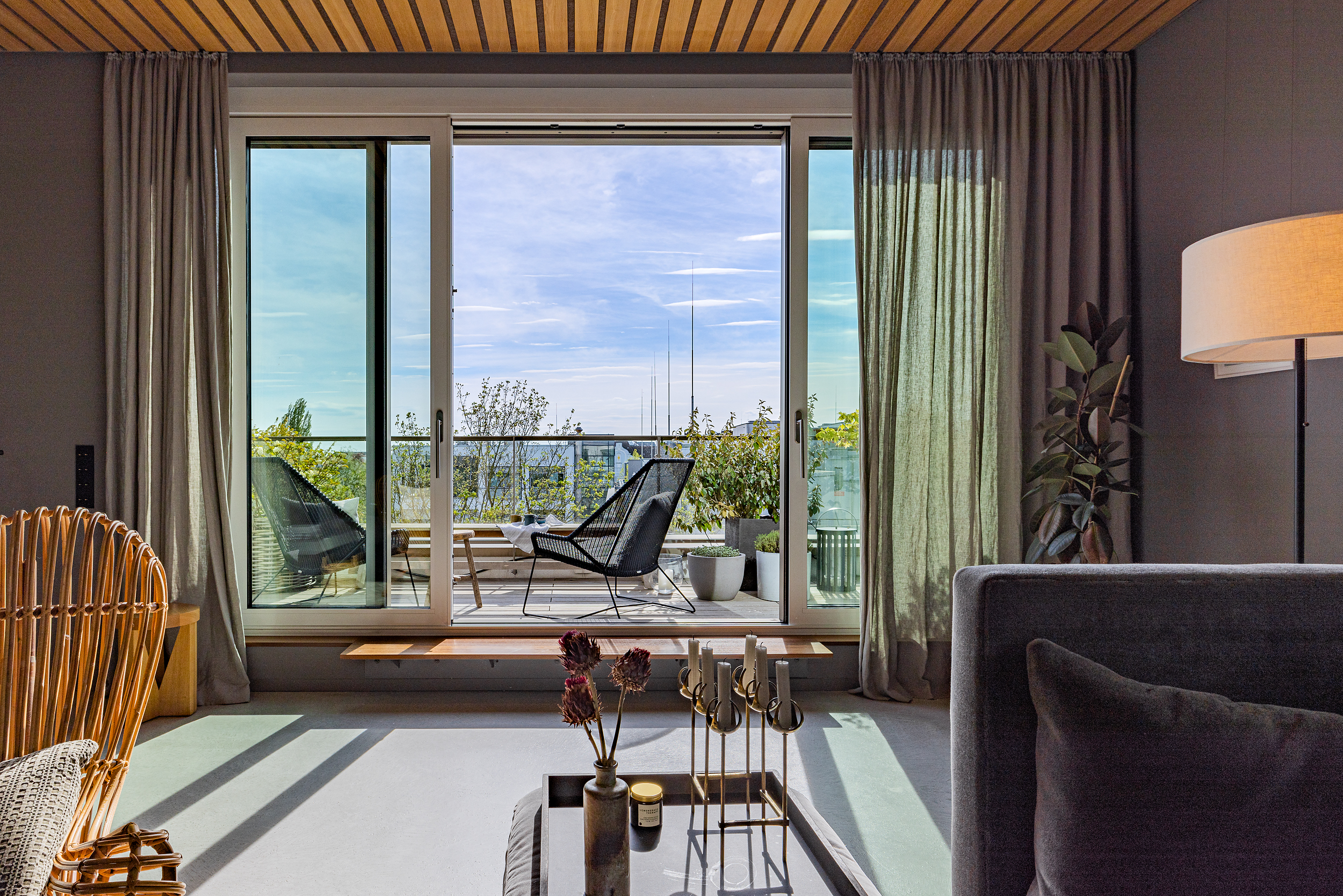 Wohnzimmer mit Glas-Schiebetür und Blick auf einen Balkon mit zwei Stühlen und Pflanzen.