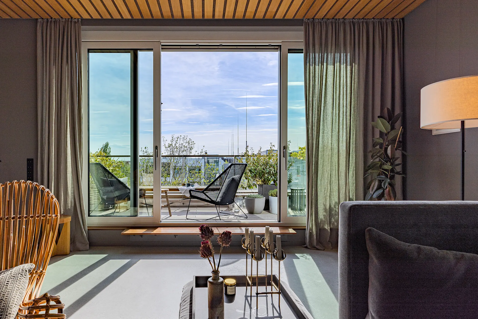 Wohnzimmer mit Glas-Schiebetür und Blick auf einen Balkon mit zwei Stühlen und Pflanzen.