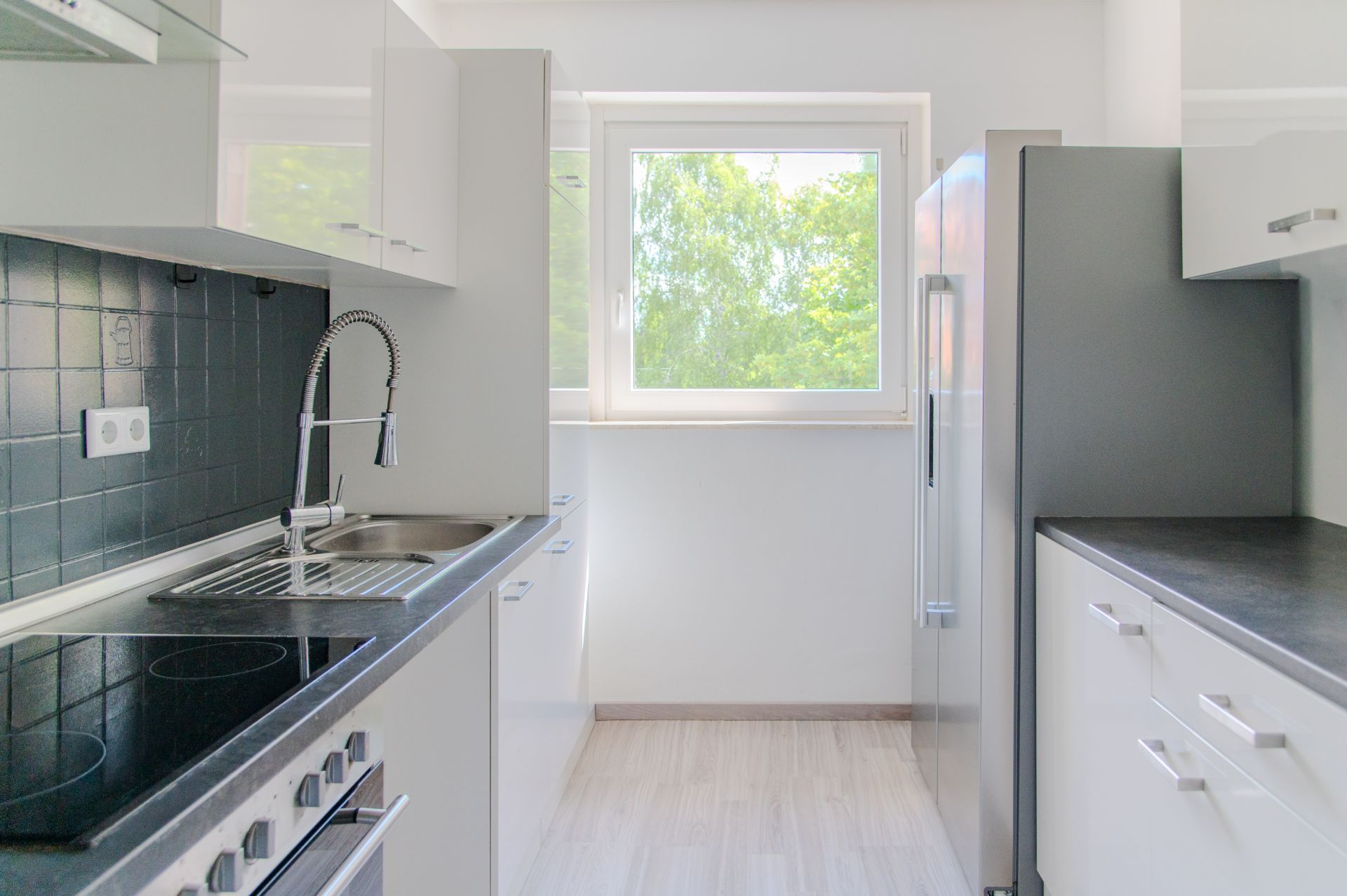 Helle Einbauküche mit Fenster, Herd, Spüle und Kühlschrank.