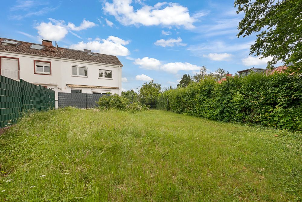 Garten mit Rasenfläche neben einem weißen Wohnhaus und grüner Hecke.