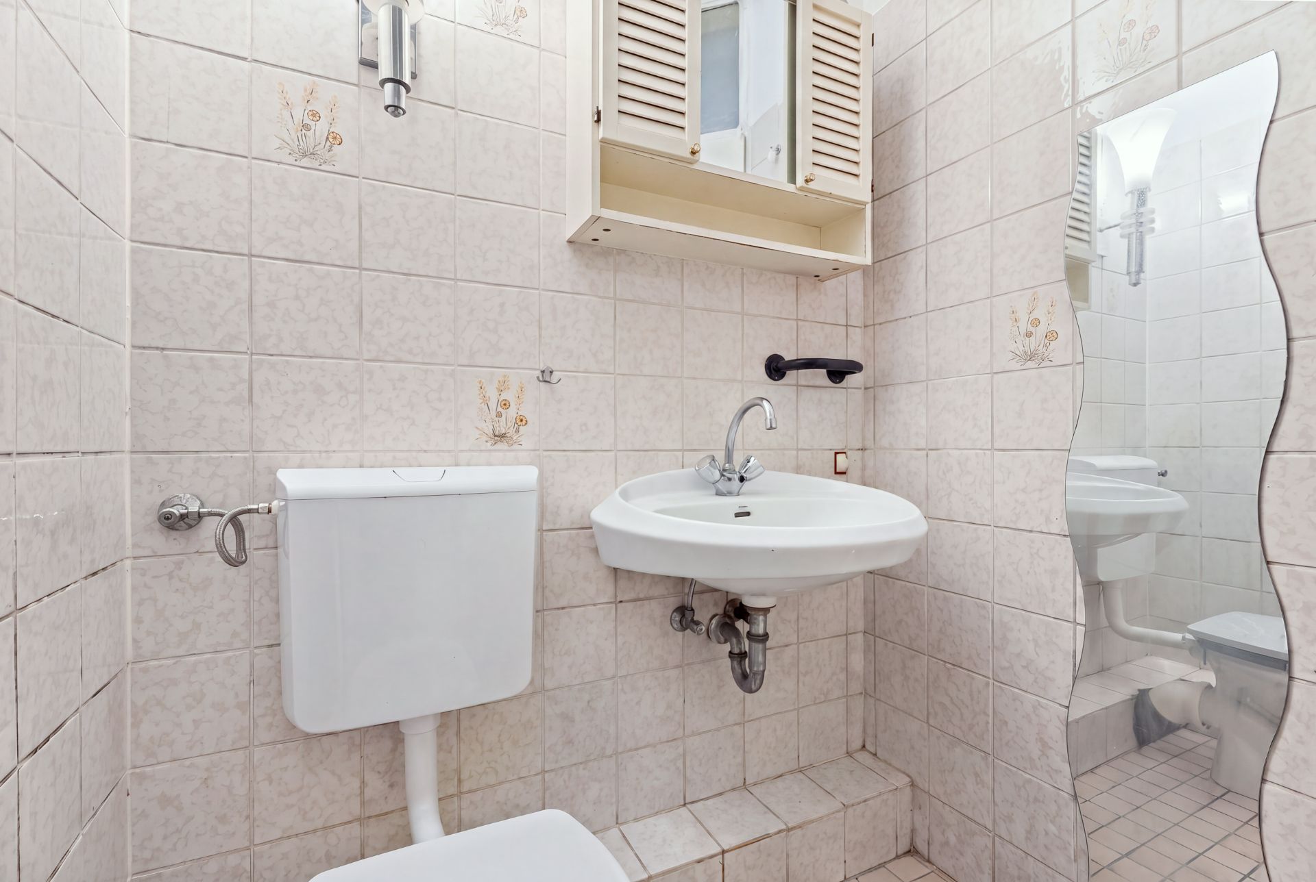 Kleines Badezimmer mit Toilette, Waschbecken, Wandspiegel und Hängeschrank.