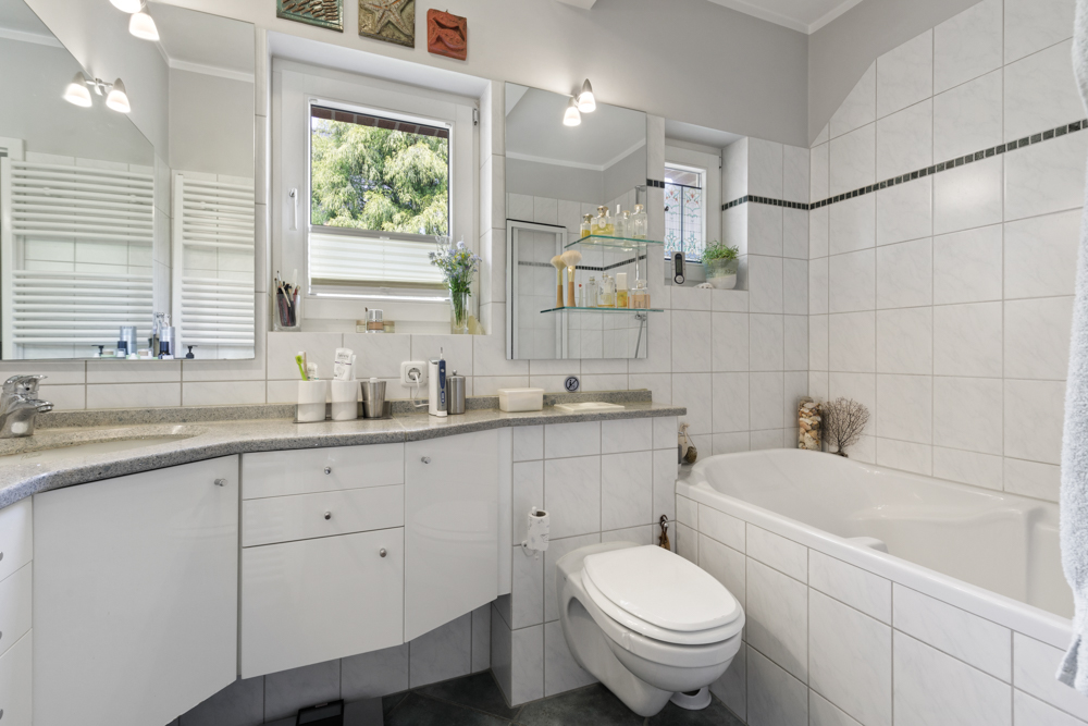Modernes Badezimmer mit Badewanne, Wandspiegeln, Waschbecken und großem Fenster.