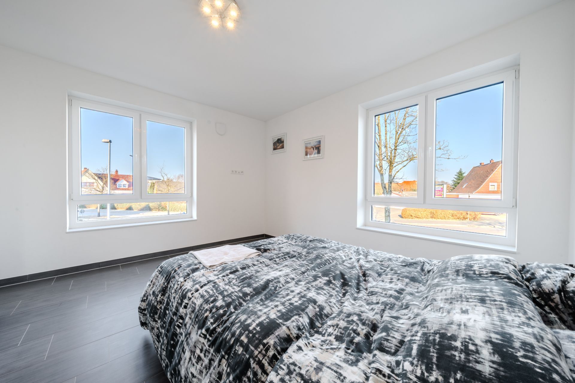 Helles Schlafzimmer mit großem Fenster, Bett und modernem Bodenbelag.