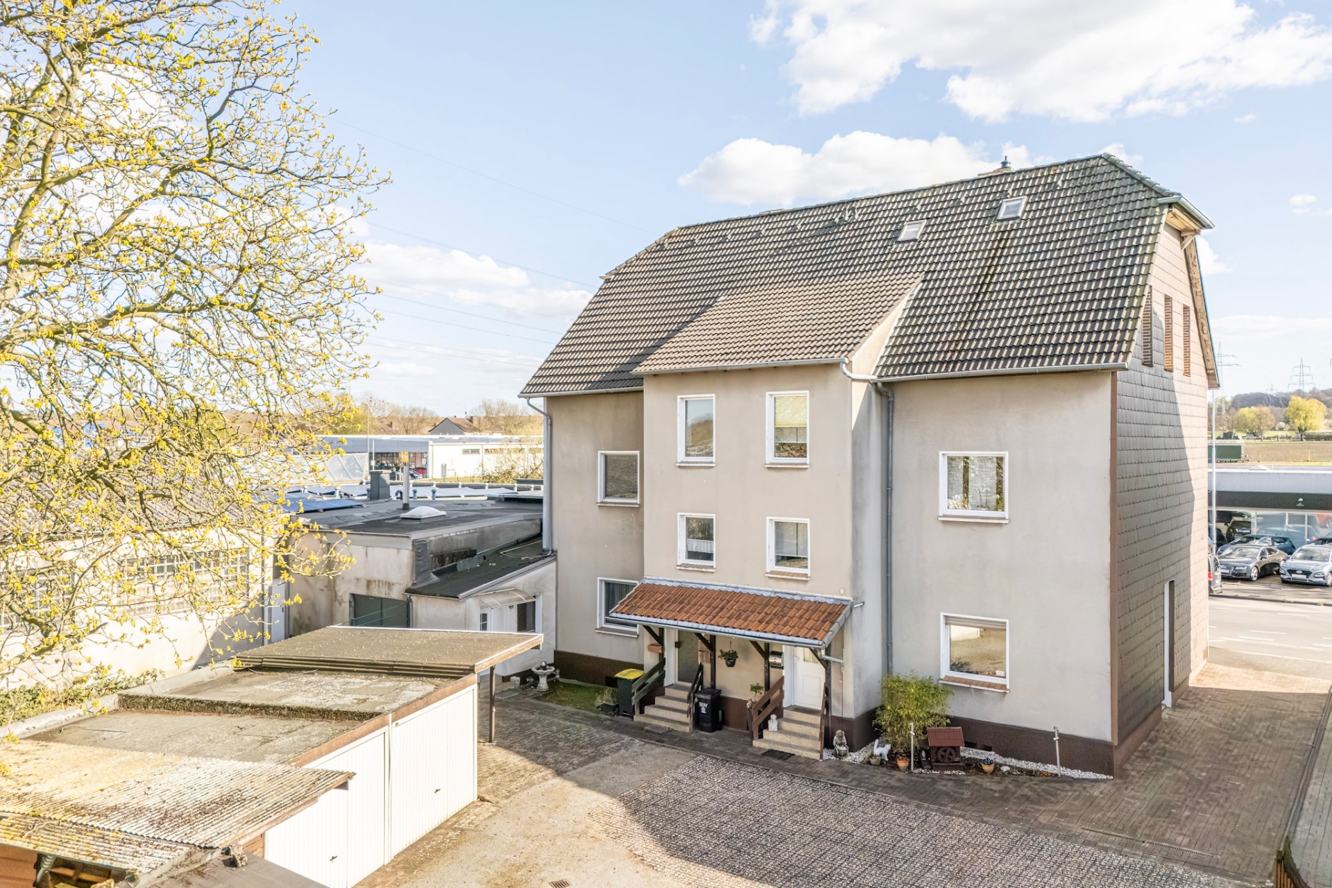 Mehrstöckiges Wohngebäude mit Satteldach und mehreren Fenstern, davor gepflasterter Hof.