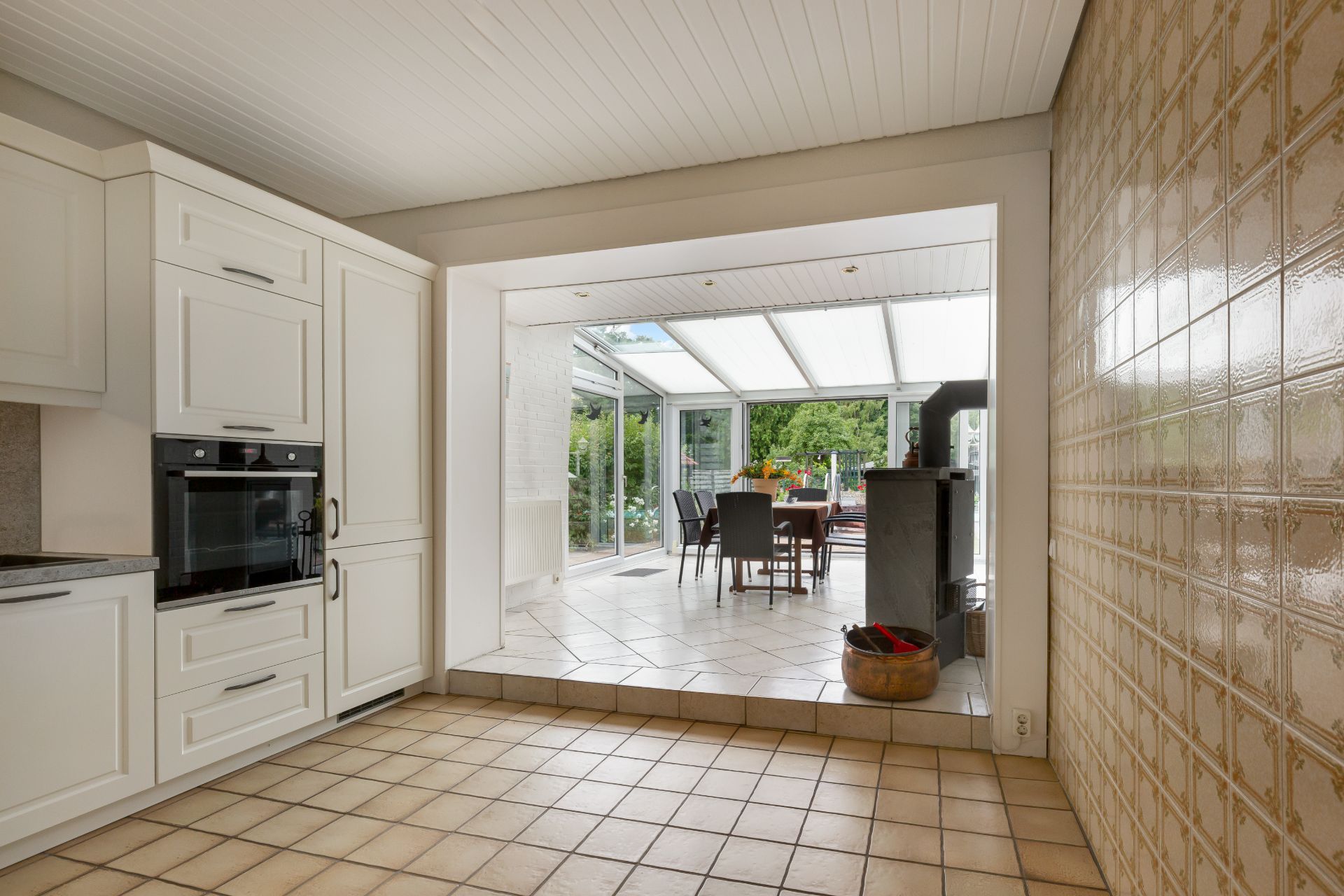 Helle Küche mit Blick auf ein Esszimmer mit Glaswänden und Garten im Hintergrund.