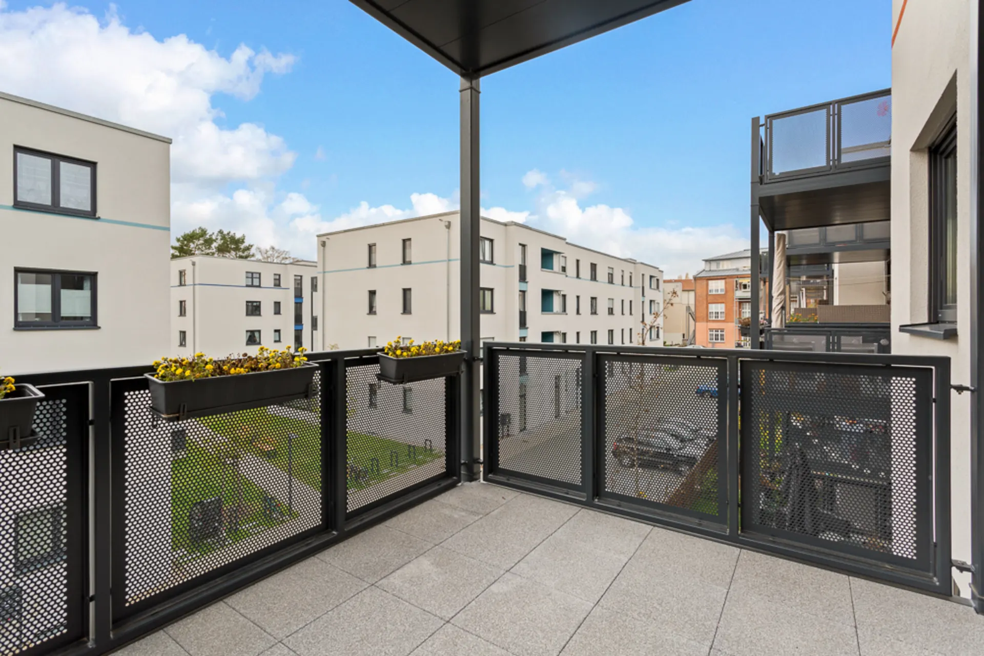Balkon mit Metallgeländer und Blumenkästen, Blick auf moderne Wohngebäude.