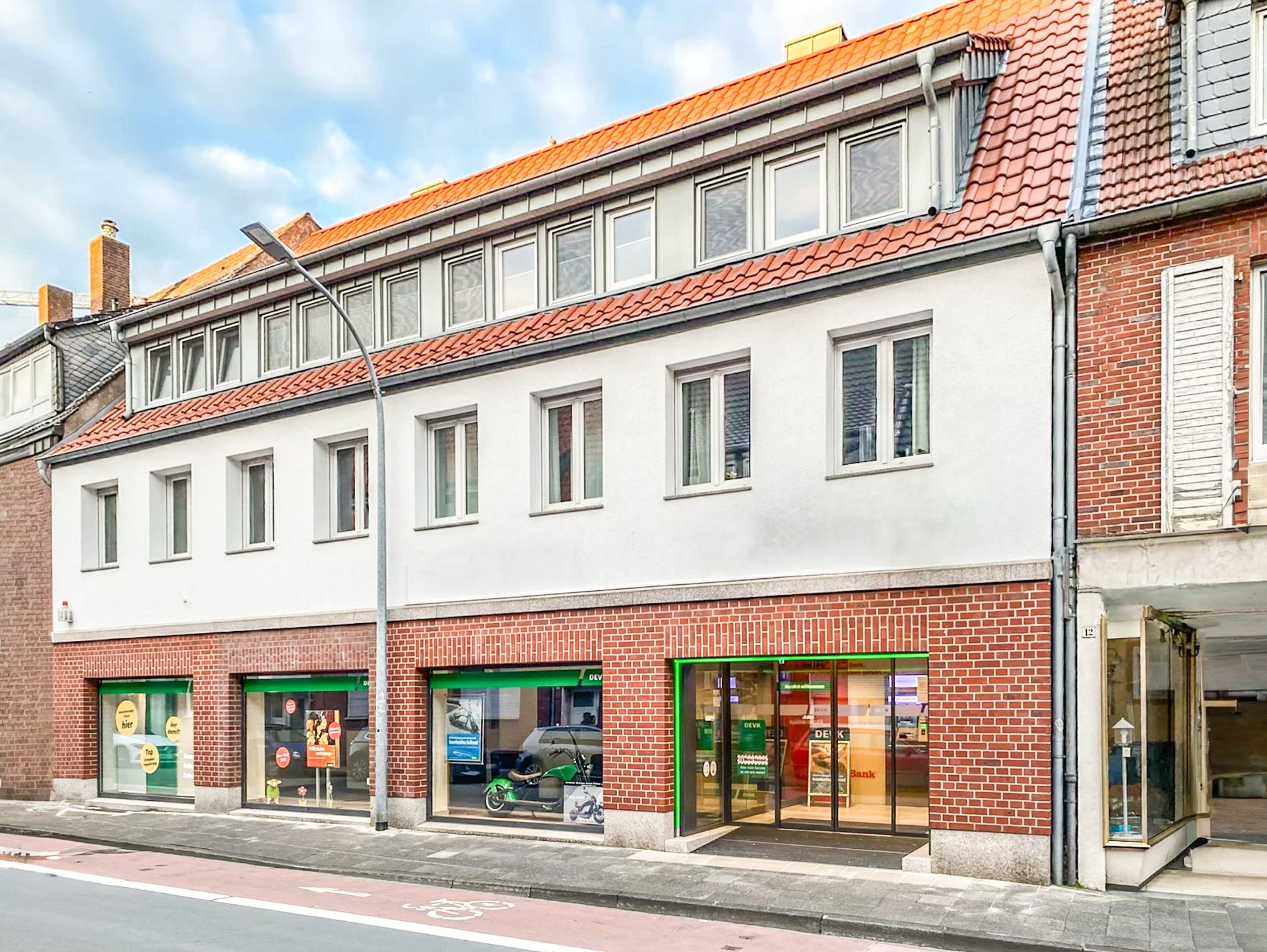 Mehrstöckiges Wohngebäude mit weißer Fassade, roten Dachziegeln und Ladengeschäften im Erdgeschoss.