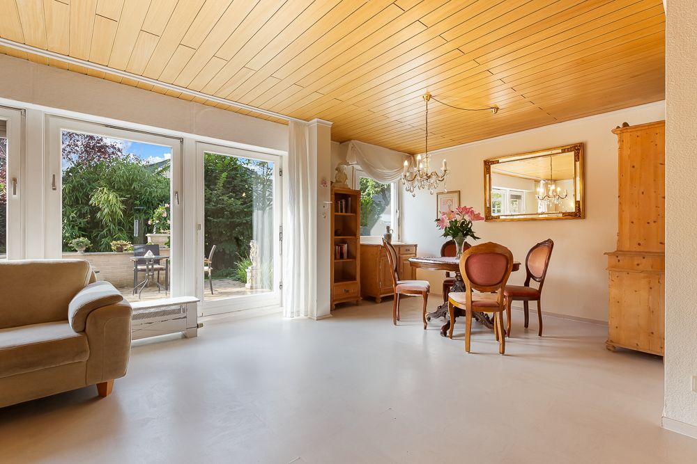 Helles Wohnzimmer mit Holzmöbeln, Esstisch, Sofa und großen Fenstern mit Blick auf den Garten.