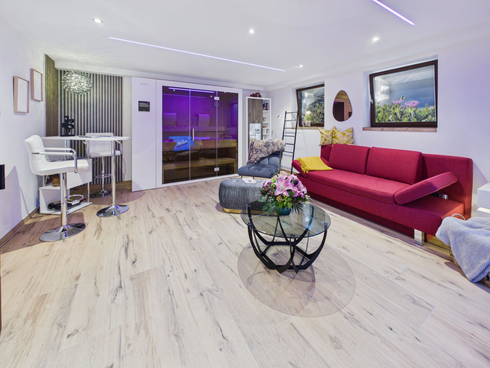 Modernes Wohnzimmer mit rotem Sofa, Glastisch, Barbereich und Glasabtrennung, helle Holzböden.