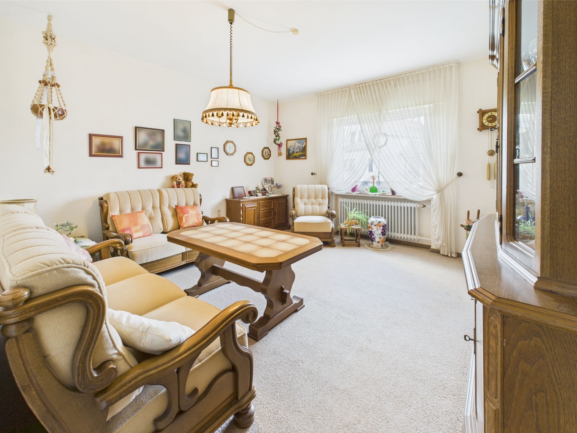 Helles Wohnzimmer mit Polstermöbeln, Couchtisch, Teppich und großem Fenster mit Gardinen.