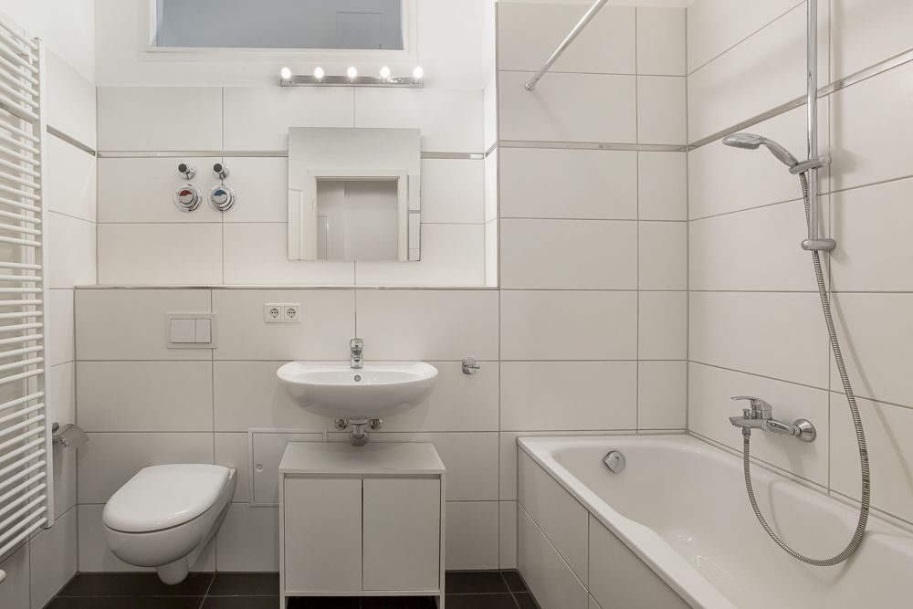 Modernes Badezimmer mit Badewanne, Waschbecken, Spiegel, WC und weißen Fliesen.
