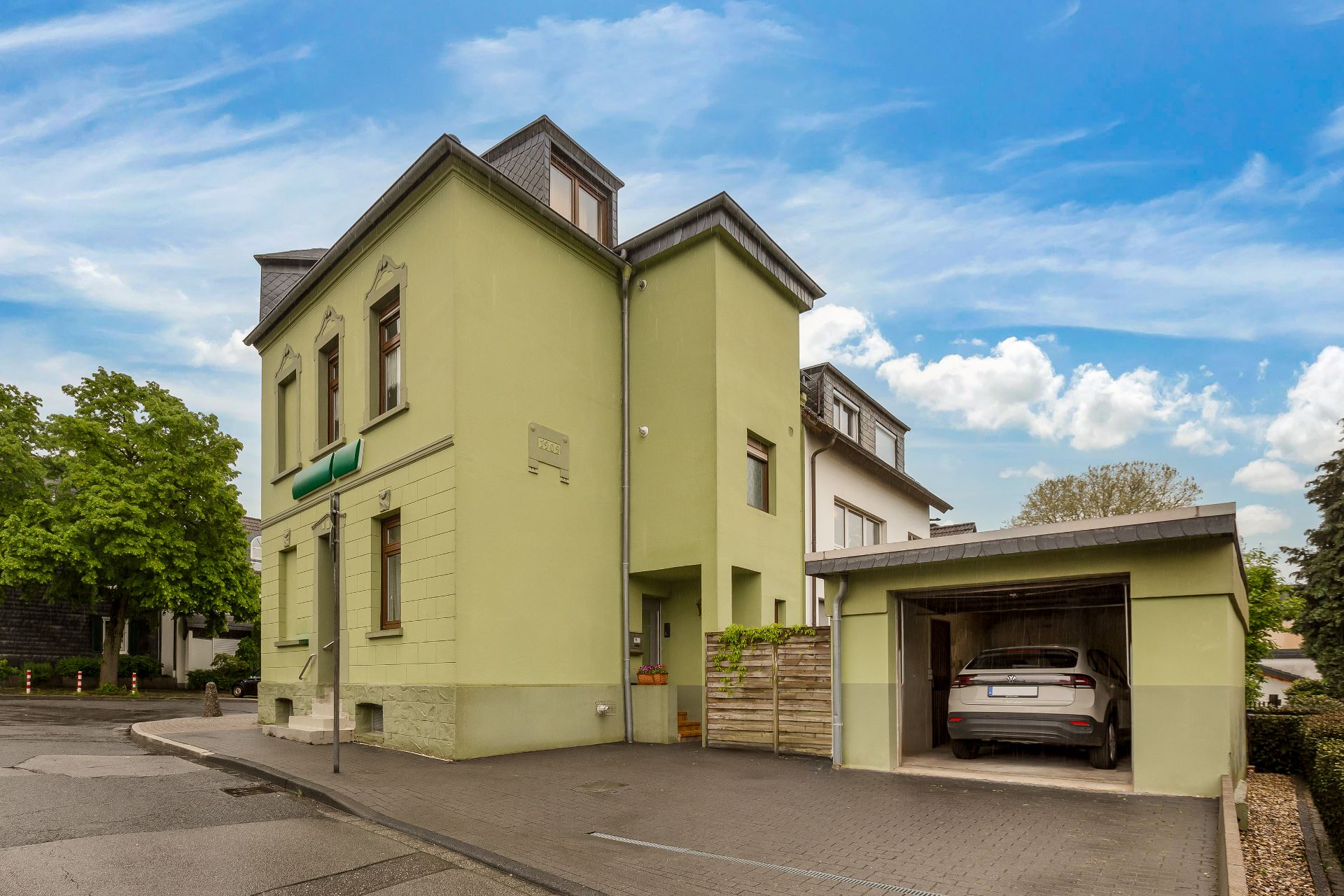 Grünes Wohnhaus mit angebauter Garage und Auto, Aufnahme von außen an einer Straßenecke.