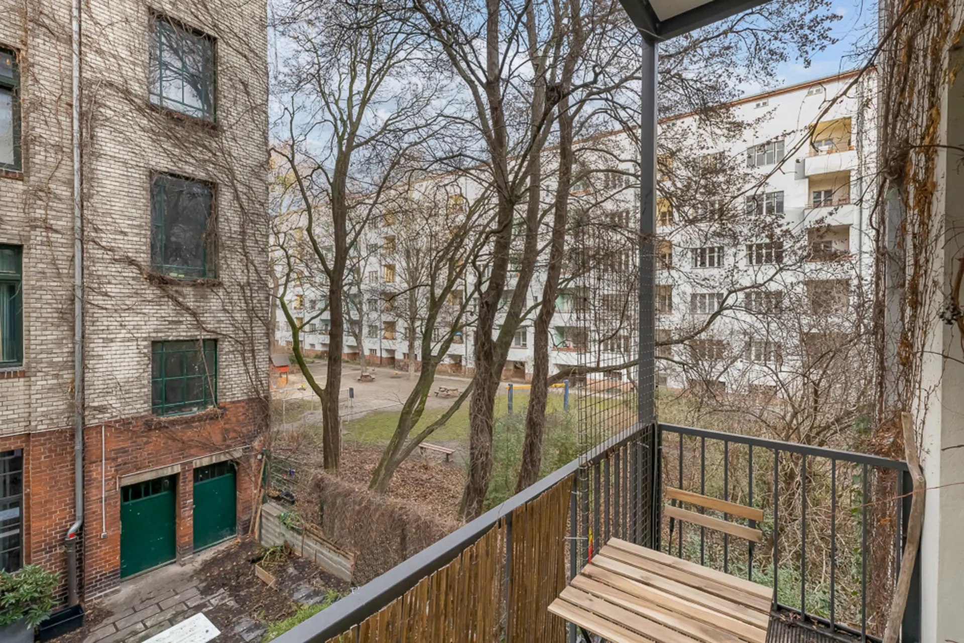 Blick von einem Balkon auf einen Innenhof mit Bäumen und umgebenden Wohngebäuden.