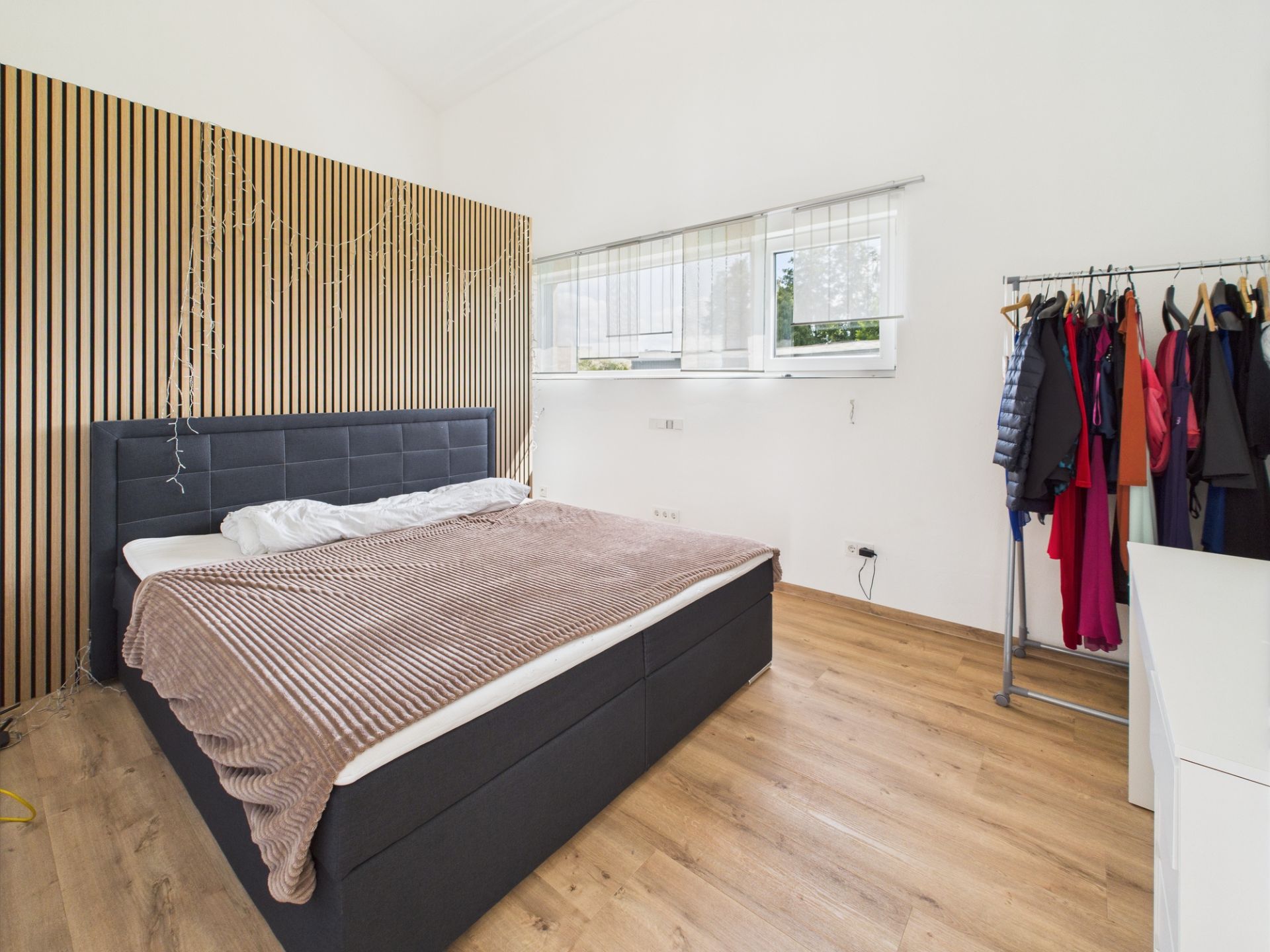 Helles Schlafzimmer mit großem Bett, Holzlamellenwand und offener Kleiderstange.