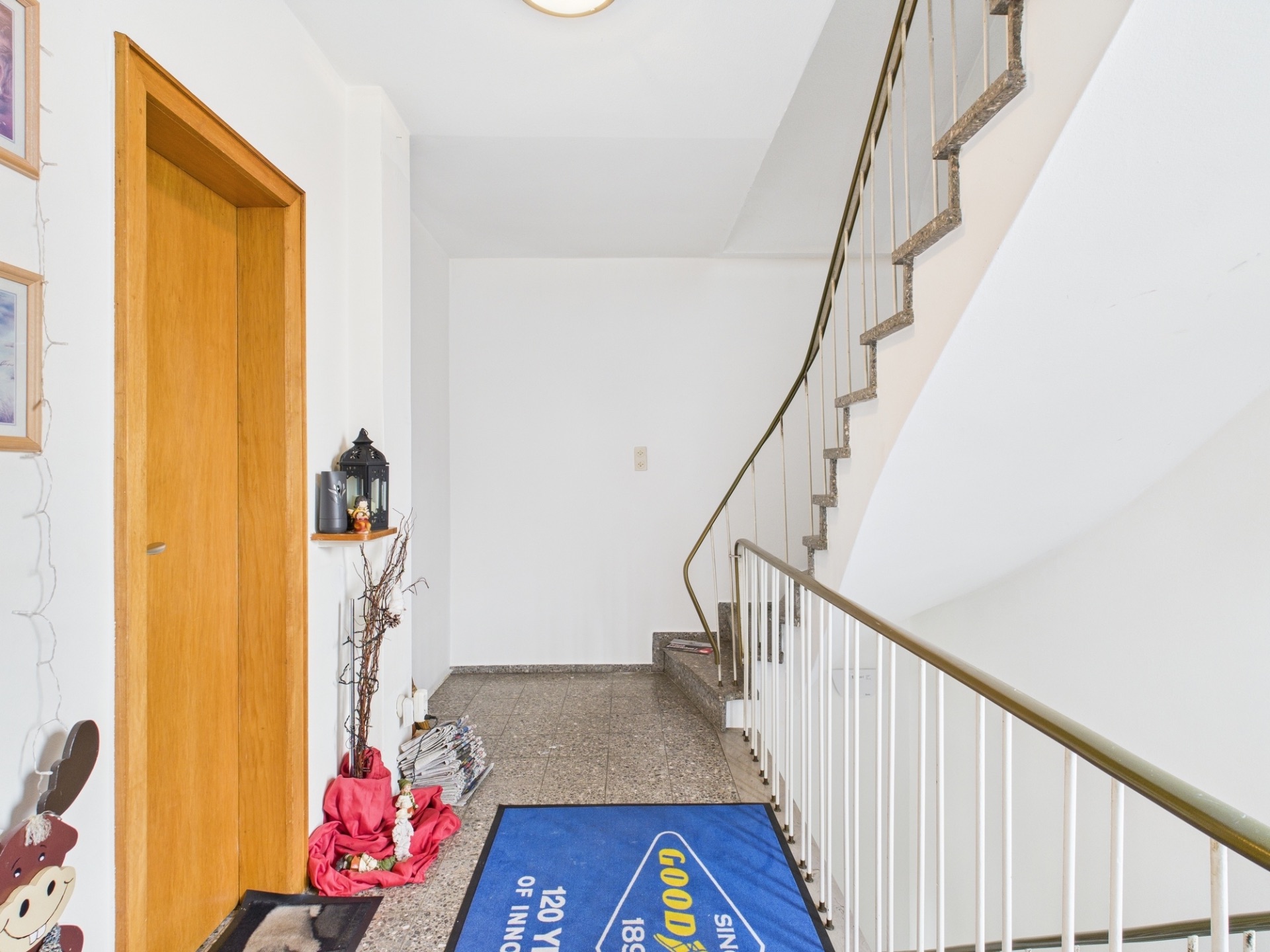 Heller Flur mit Treppe, Holztür und blauer Fußmatte in einem Wohnhaus.