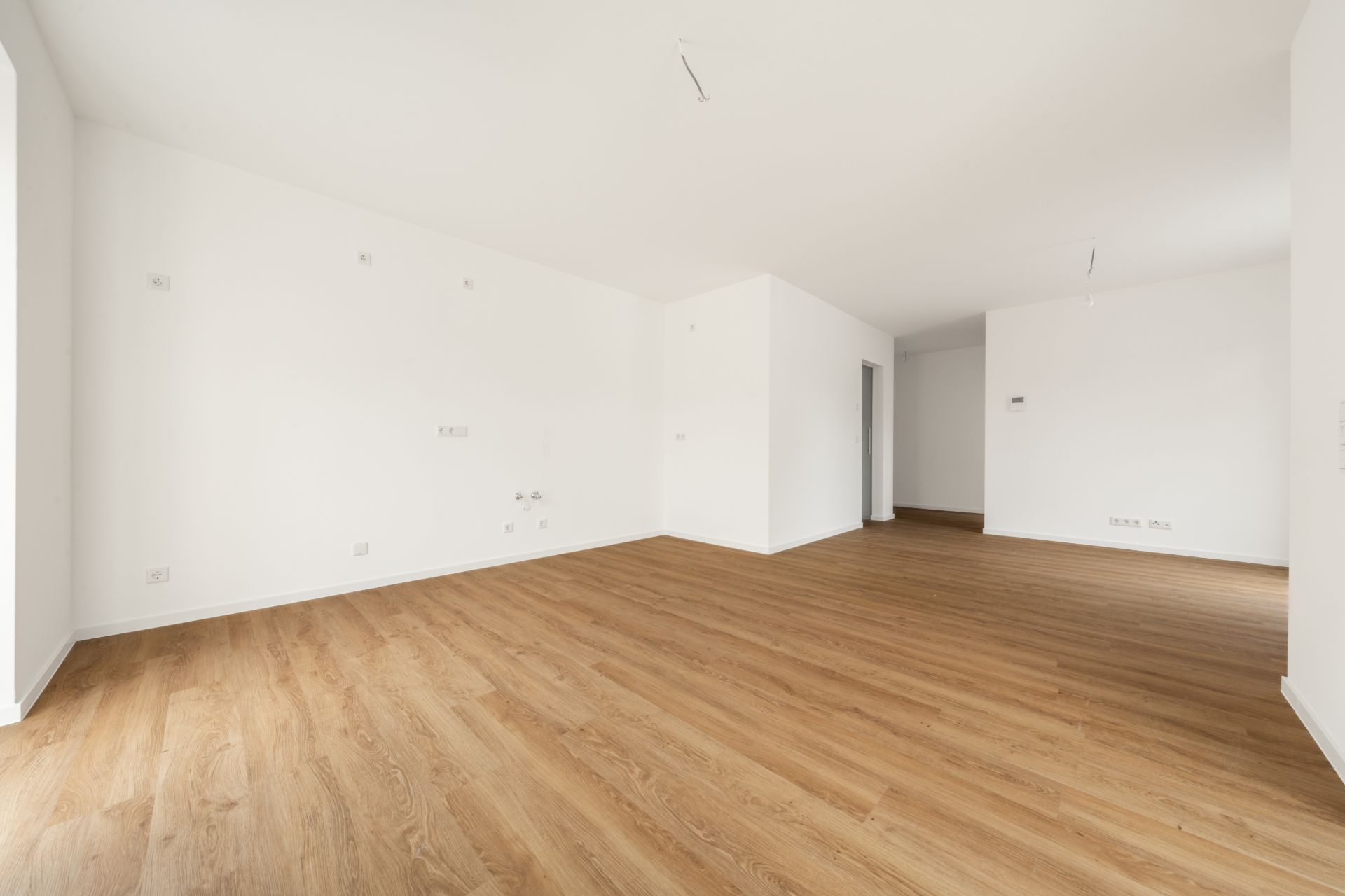 Leerer Raum mit weiß gestrichenen Wänden und hellem Holzboden.