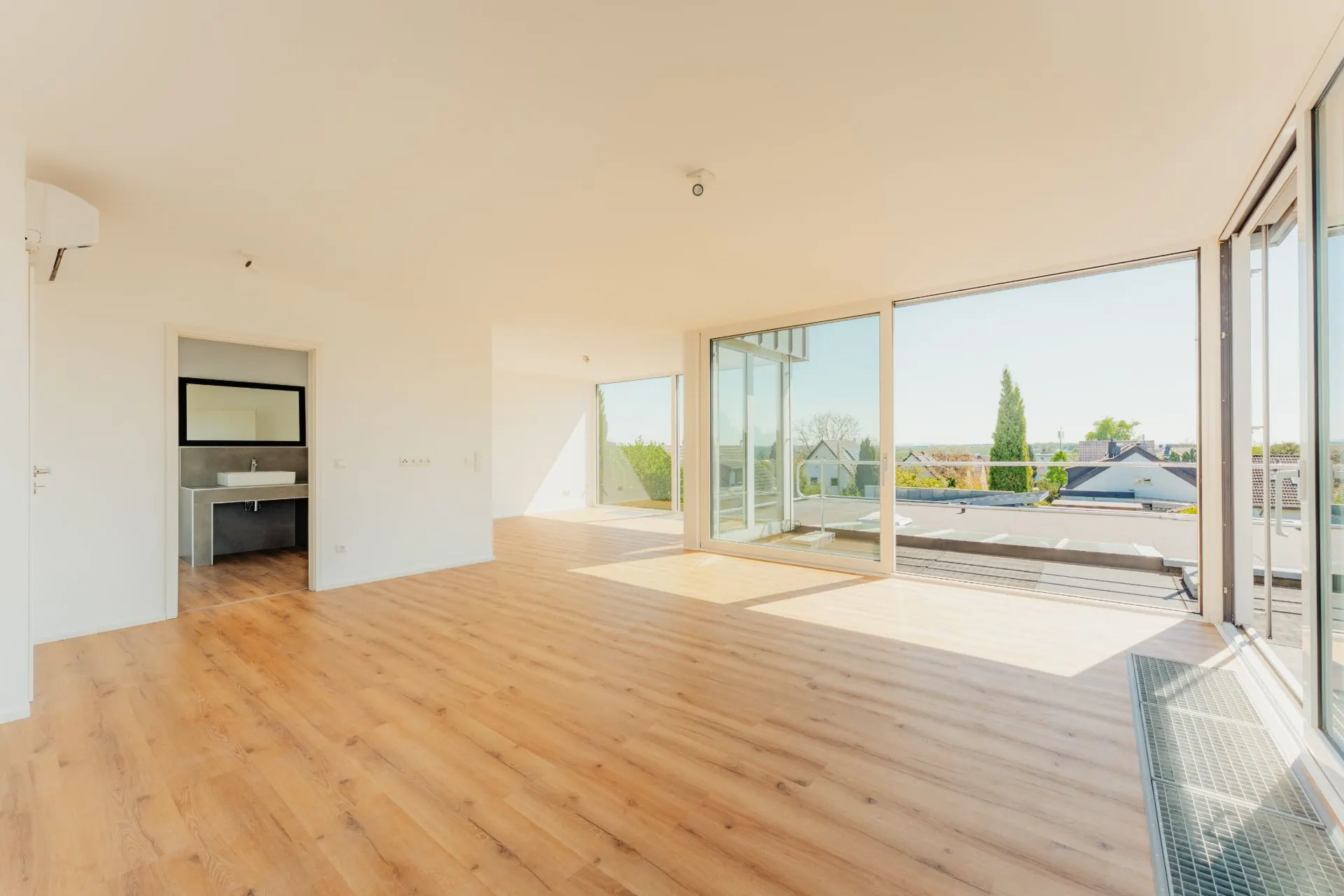 Helles Wohnzimmer mit Holzfußboden, großen Fenstern und Zugang zu einer Terrasse.