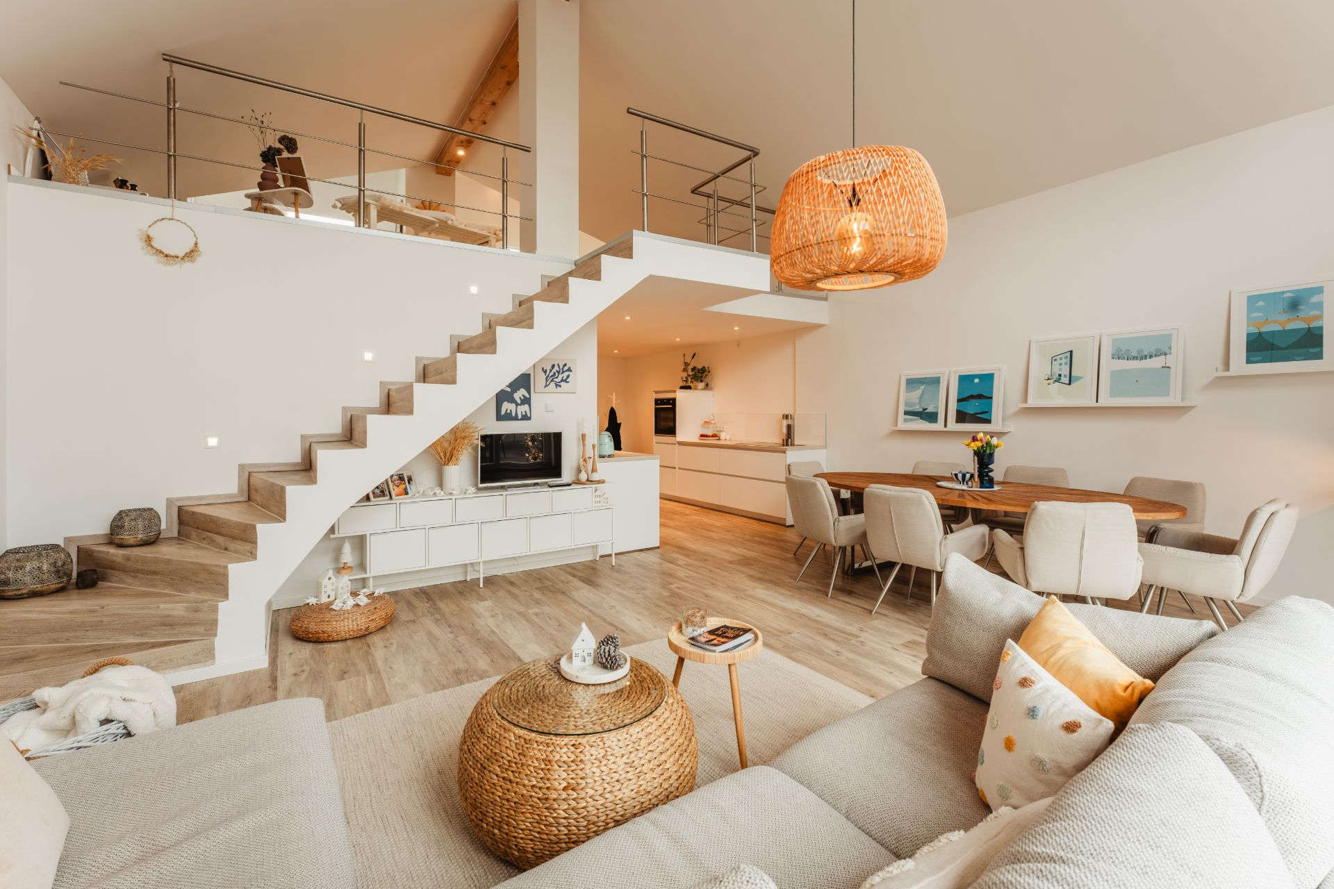 Helles Wohnzimmer mit Sofa, Esstisch, offener Küche und Holztreppe zu einer Galerie.