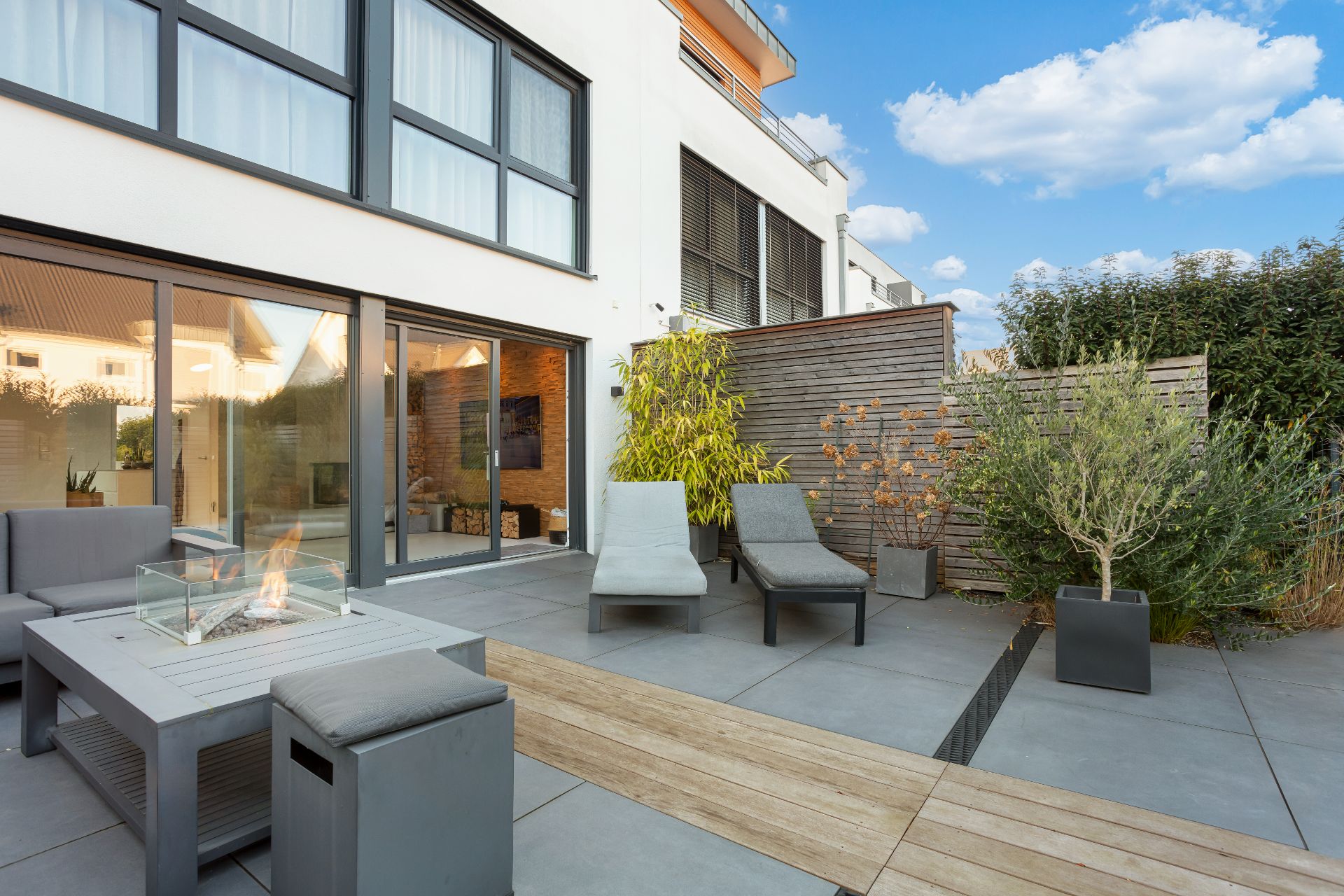 Moderne Terrasse mit Sitzmöbeln, Feuerstelle und Pflanzen vor einem Wohnhaus.