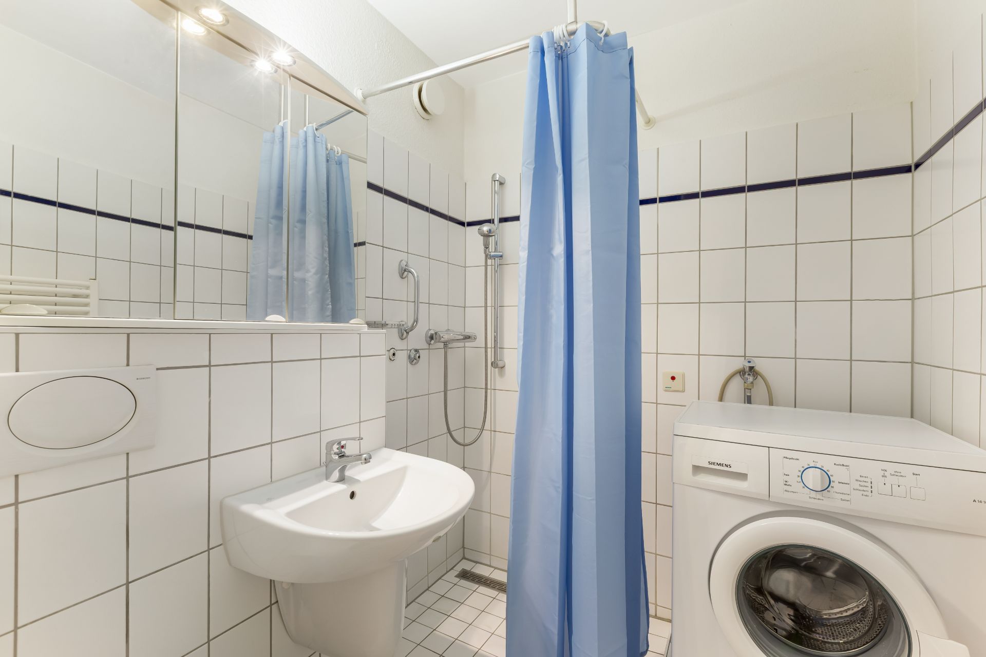 Badezimmer mit Waschbecken, Dusche mit blauem Vorhang und Waschmaschine.