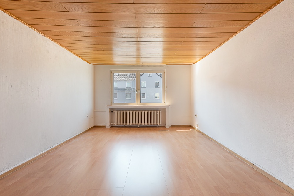 Leerer Raum mit Holzdecke, hellen Wänden, Laminatboden und Fenster mit Heizkörper.