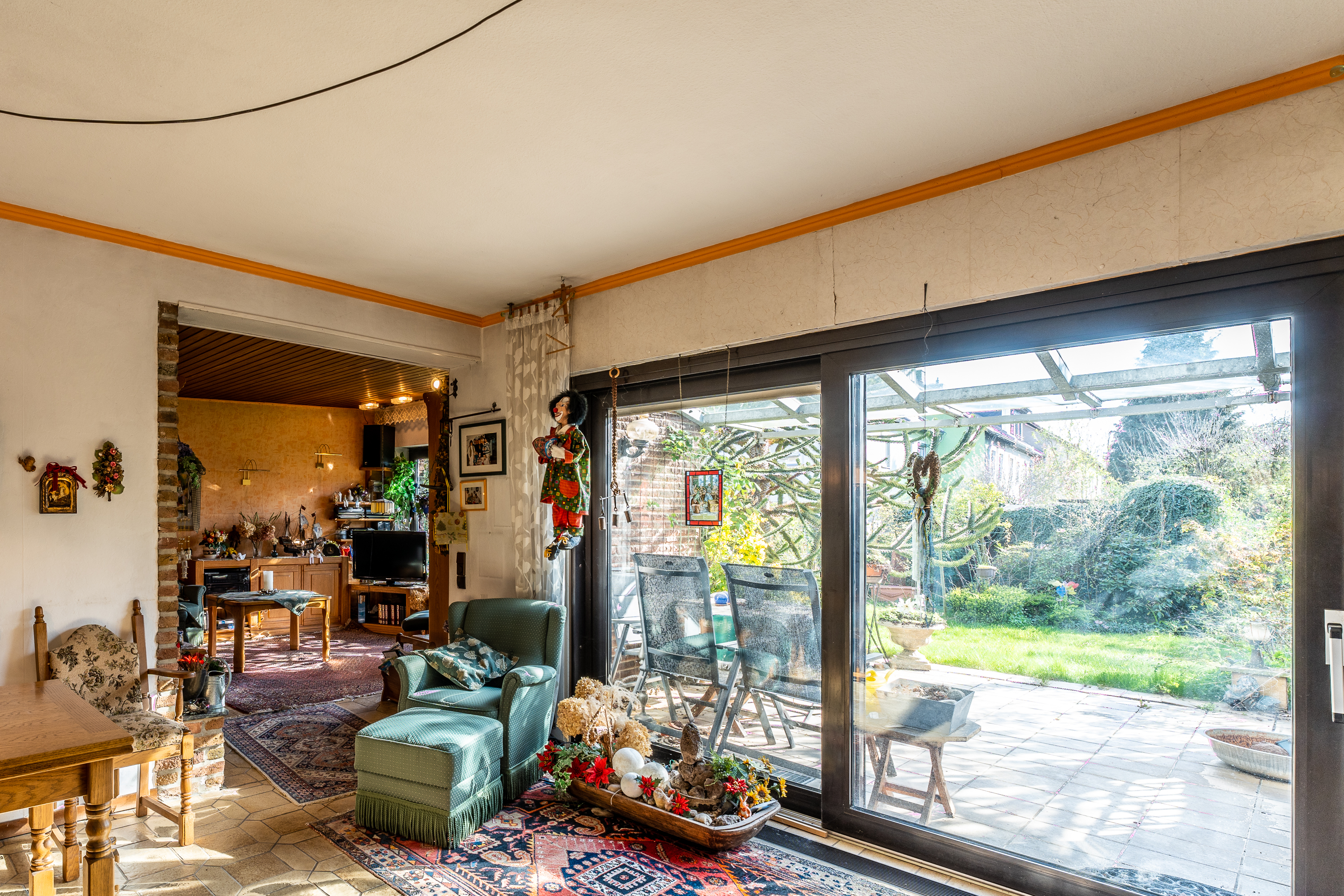 Helles Wohnzimmer mit großen Fenstern, Blick auf Terrasse und Garten, Sessel und Dekorationen sichtbar.