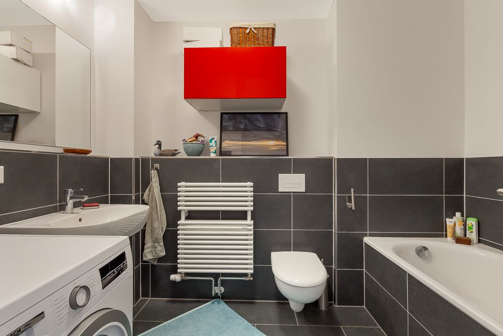 Modernes Badezimmer mit Waschmaschine, Waschbecken, Wandtoilette und Badewanne.