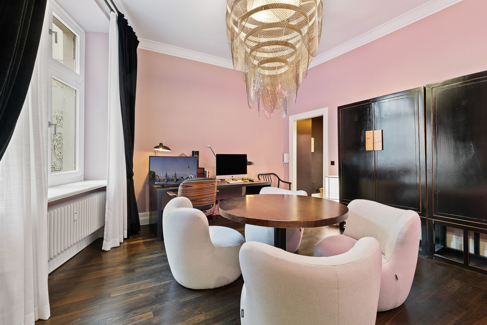 Wohnzimmer mit rundem Holztisch, vier weißen Sesseln und großem Kronleuchter.