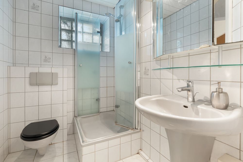 Helles Badezimmer mit Dusche, Wand-WC und Waschbecken, alles mit weißen Fliesen.