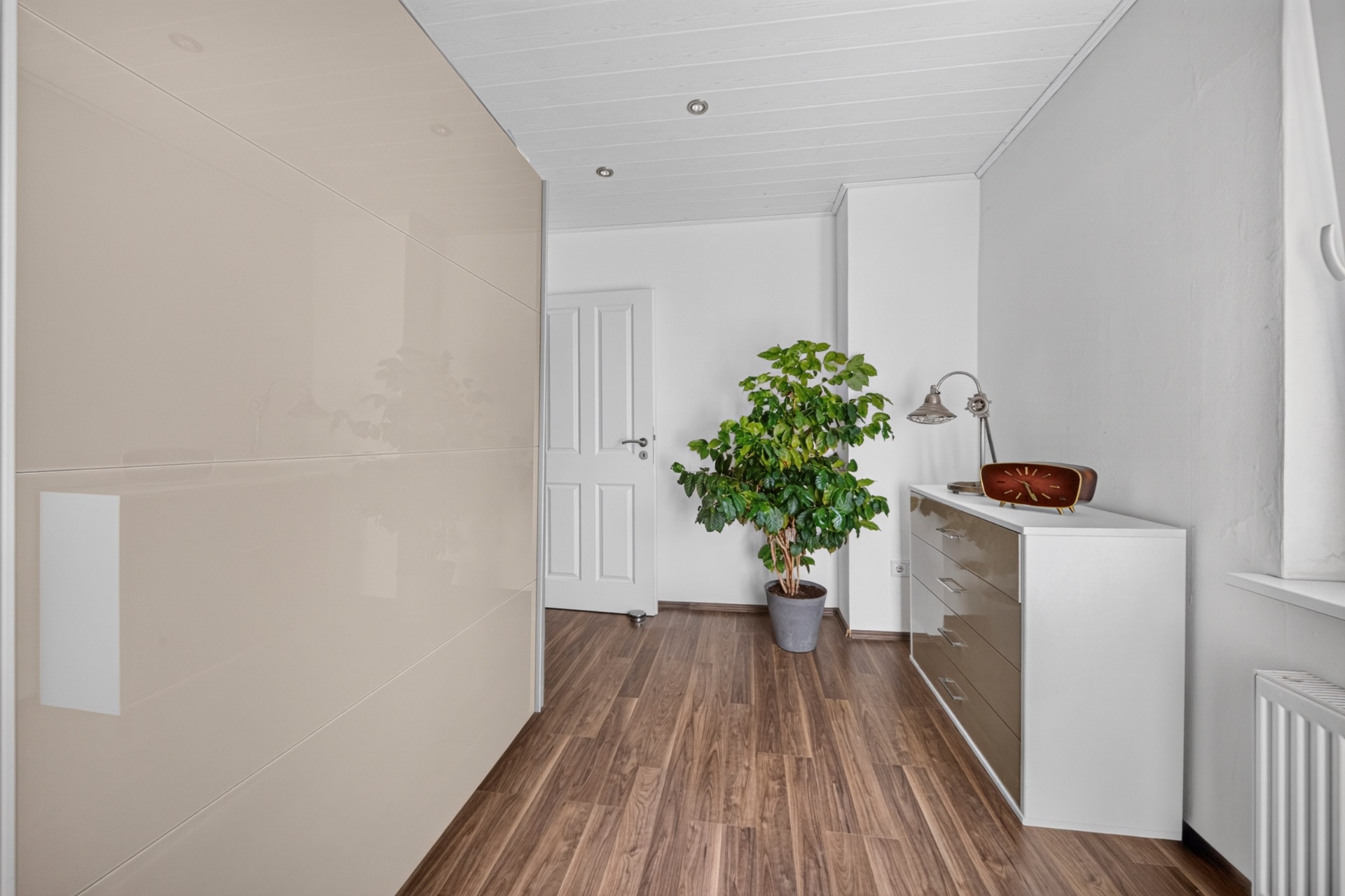 Heller Flur mit Holzfußboden, großem Schrank, Kommode und grünem Blumentopf.