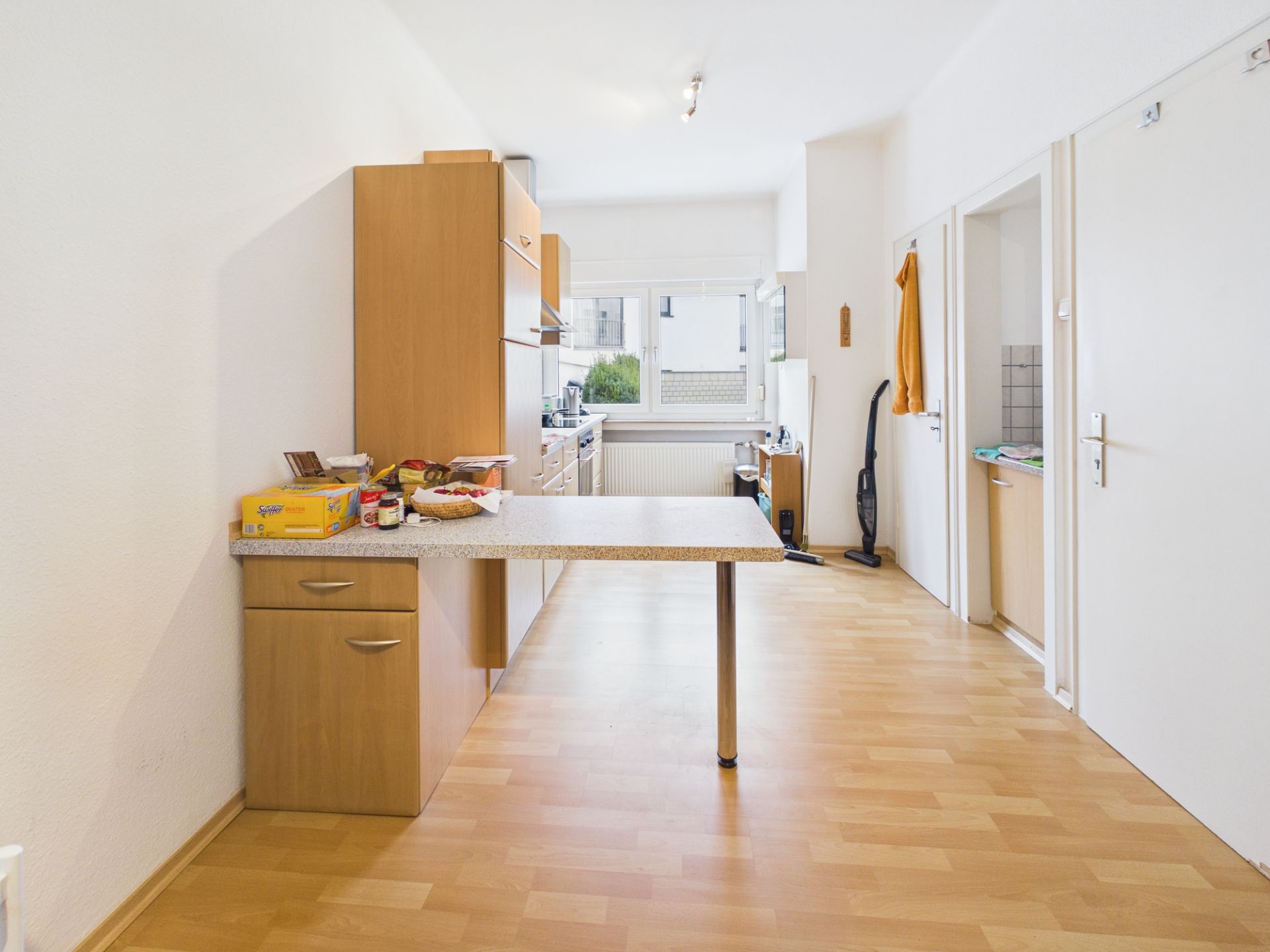 Helle Küche mit Holzboden, Küchenzeile, Esstheke und Haushaltsgeräten, Fenster im Hintergrund.