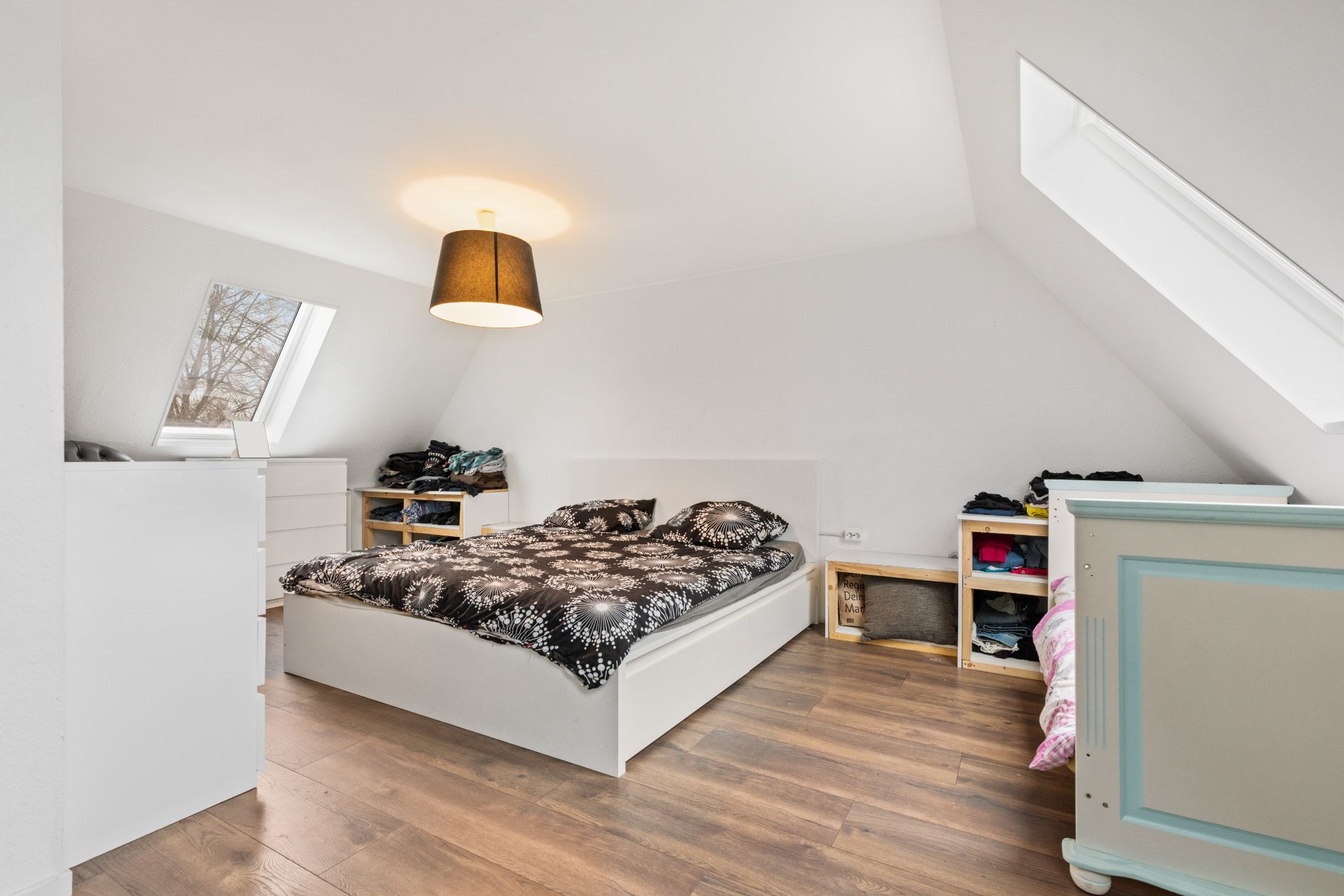 Helles Schlafzimmer mit Doppelbett, Kommoden, Holzfußboden und Dachfenstern.
