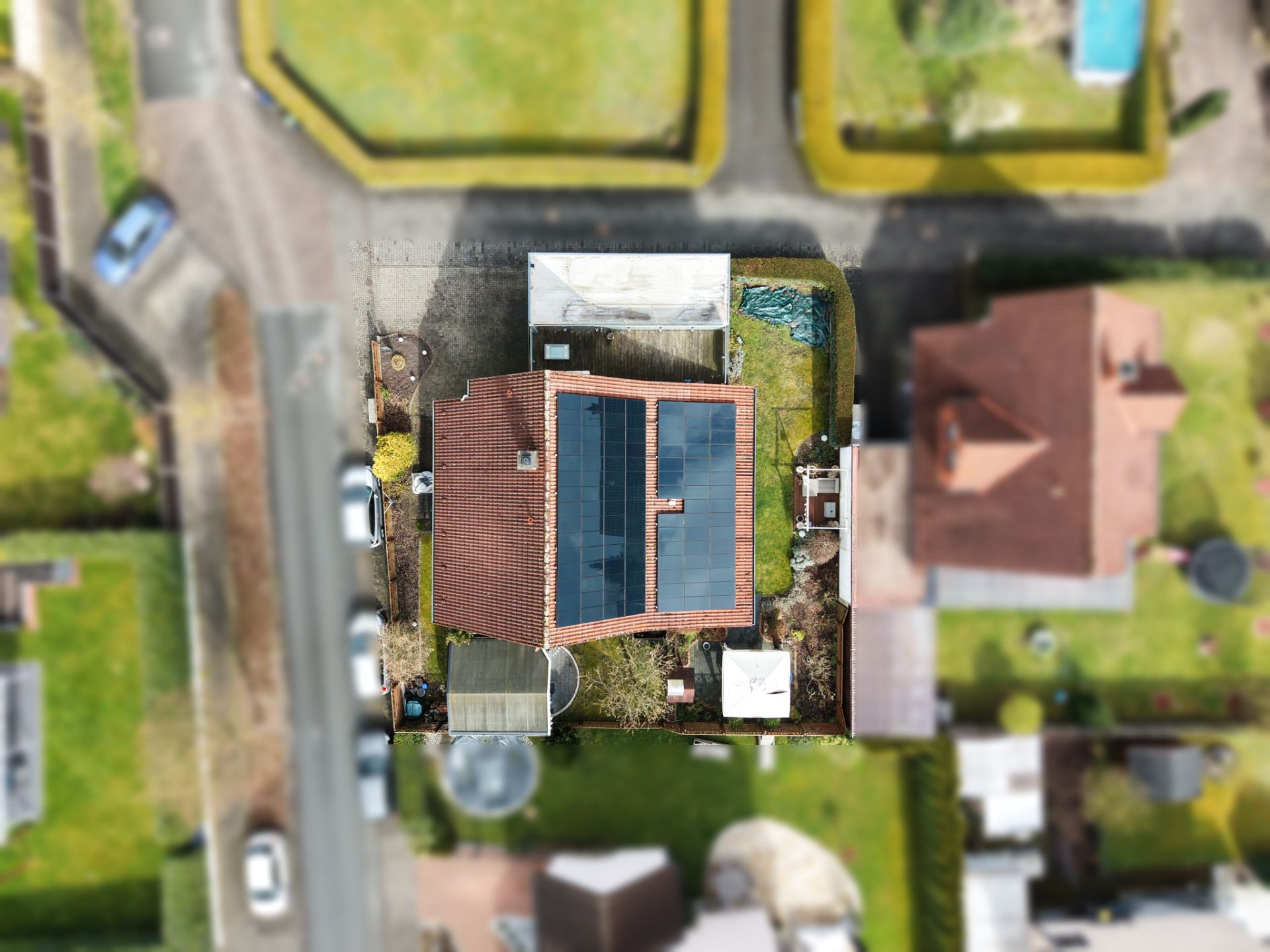 Luftaufnahme eines Hauses mit Solarpanels auf dem Dach und Garten, umgeben von anderen Häusern.
