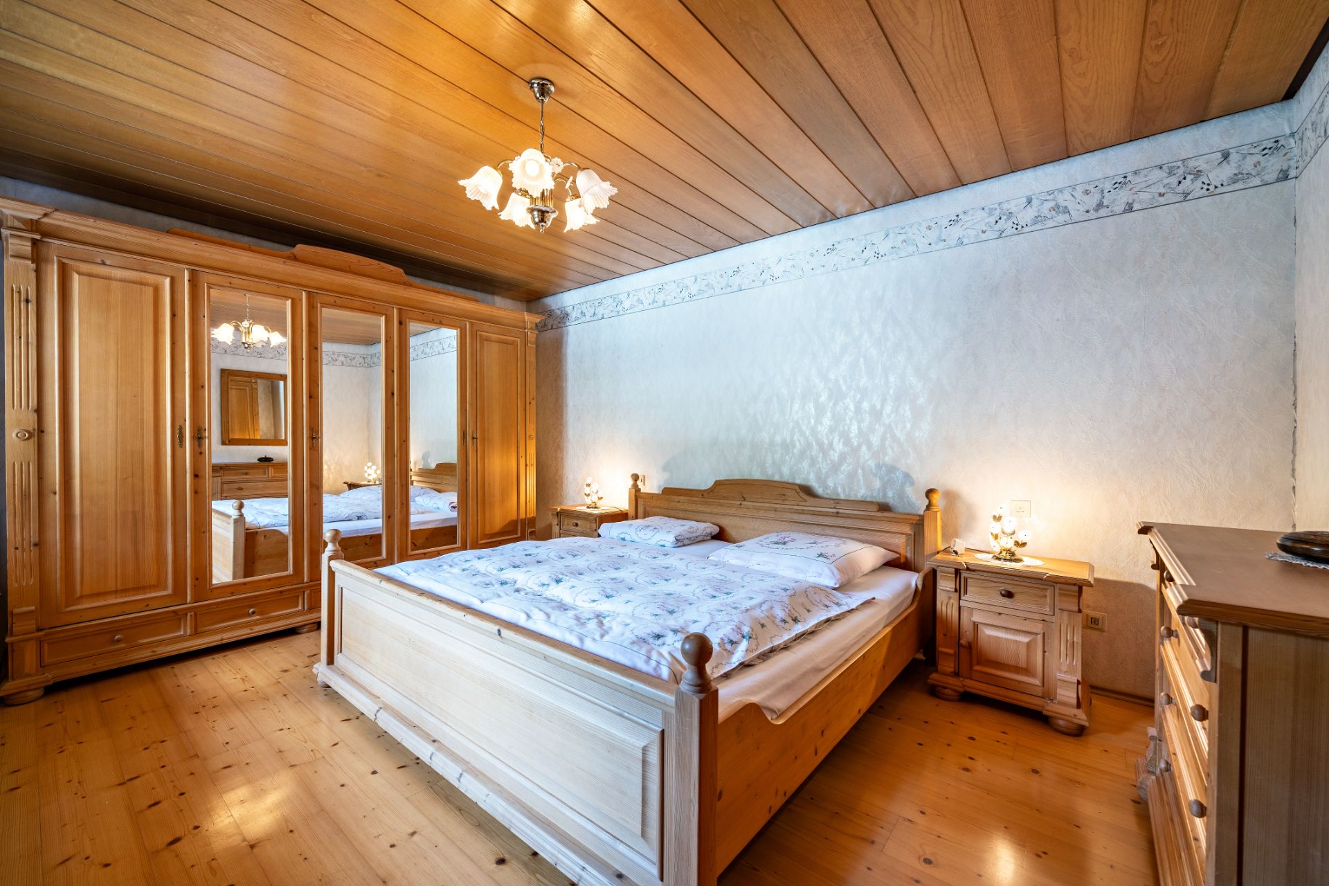 Schlafzimmer mit Holzbett, Nachttischen, großem Holzschrank mit Spiegeln und Holzdecke.