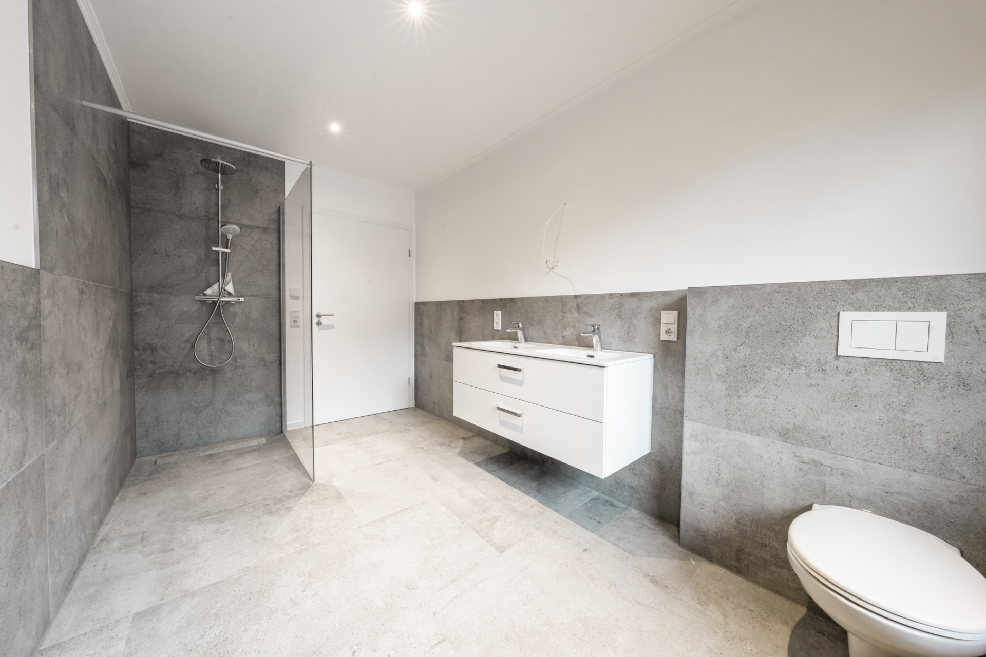 Modernes Bad mit begehbarer Dusche, Waschbecken mit Unterschrank und WC auf grauen Fliesen.